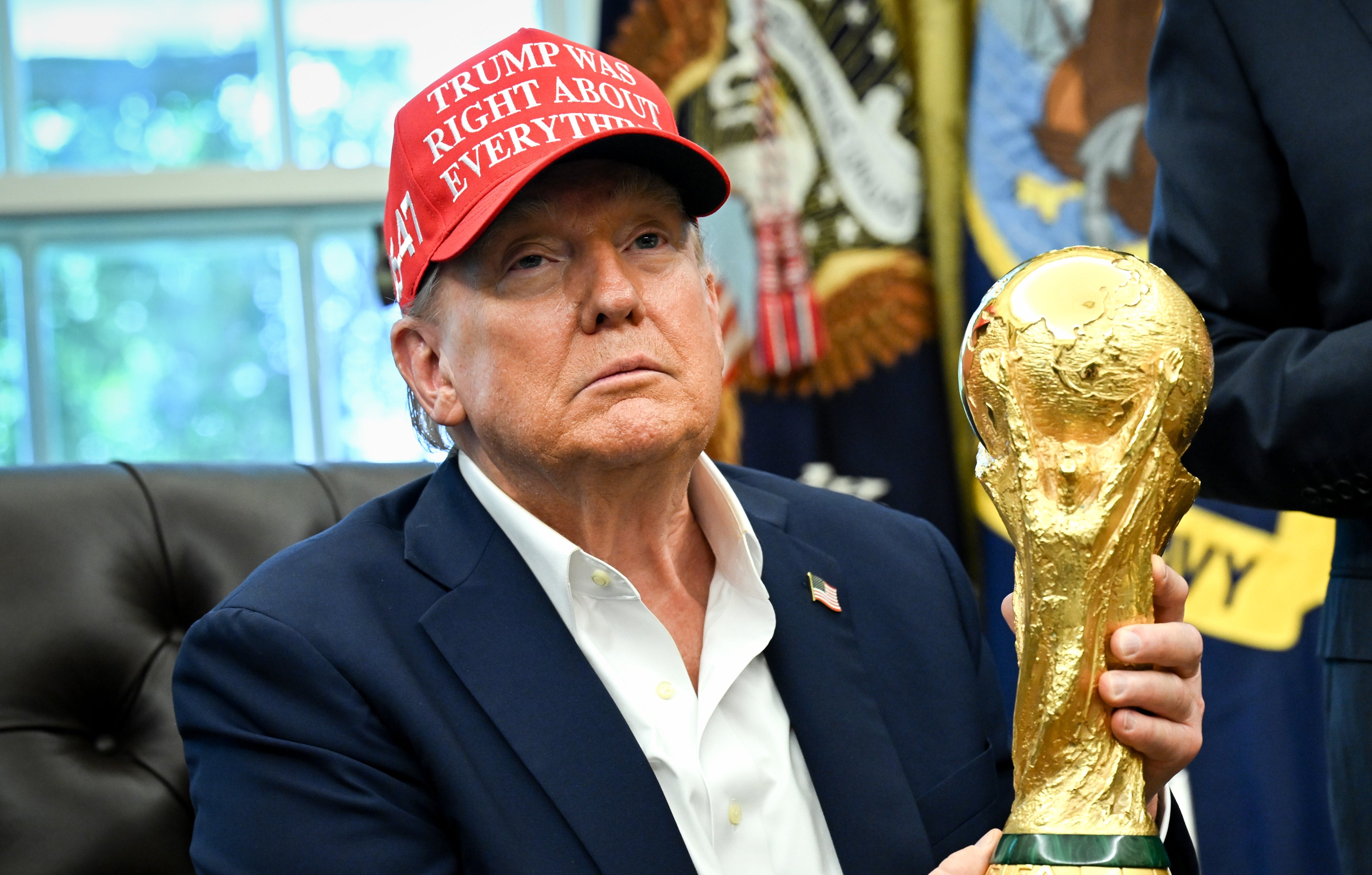 En person i en "Trump hadde rett i alt" cap holder et trofé som ligner verdensmesterskapet i et kontor med amerikanske regjeringsemblemer