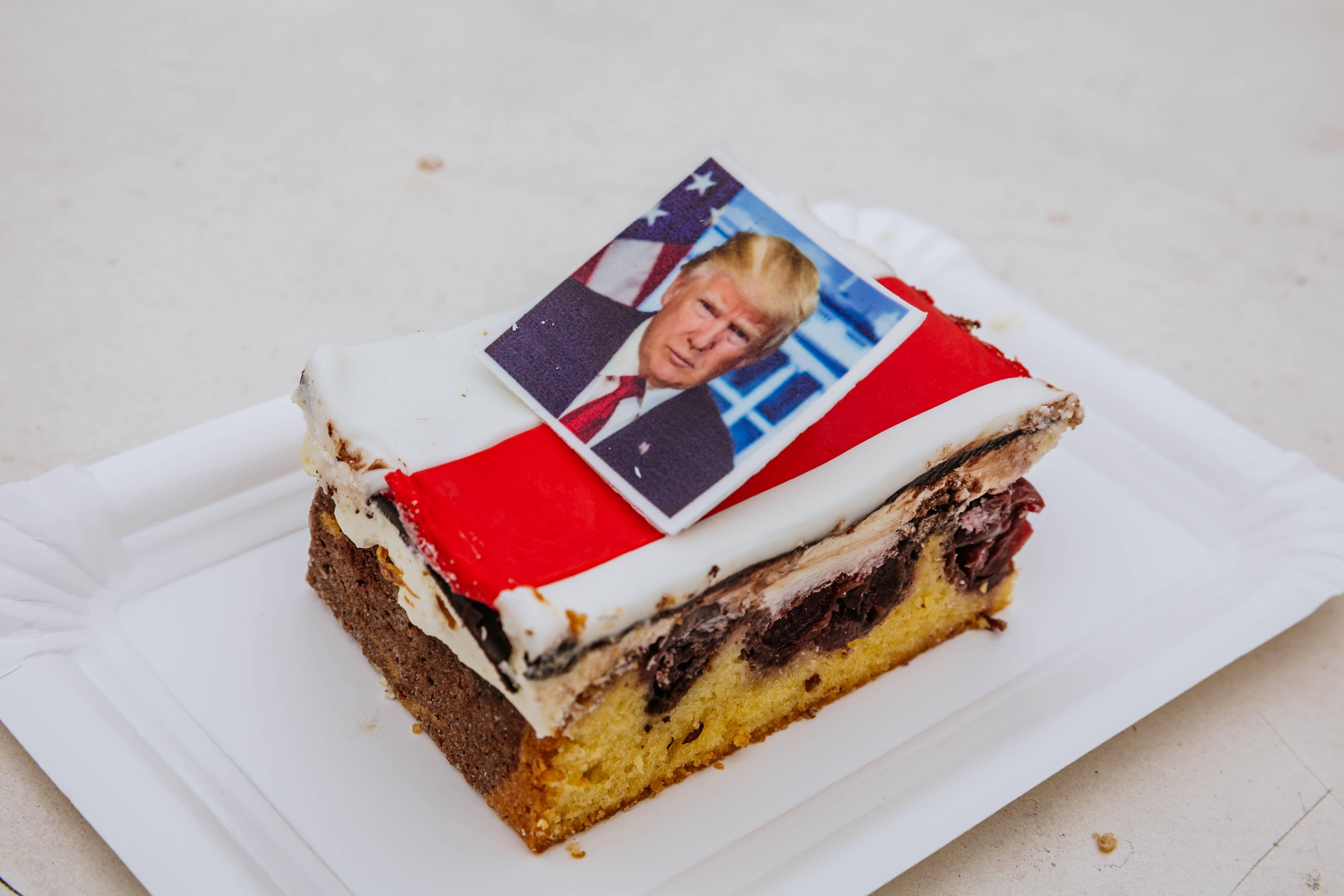 Kake med et bilde av en manns ansikt på toppen, liggende på en hvit tallerken, muligens for en politisk begivenhet eller nyhetsinnslag