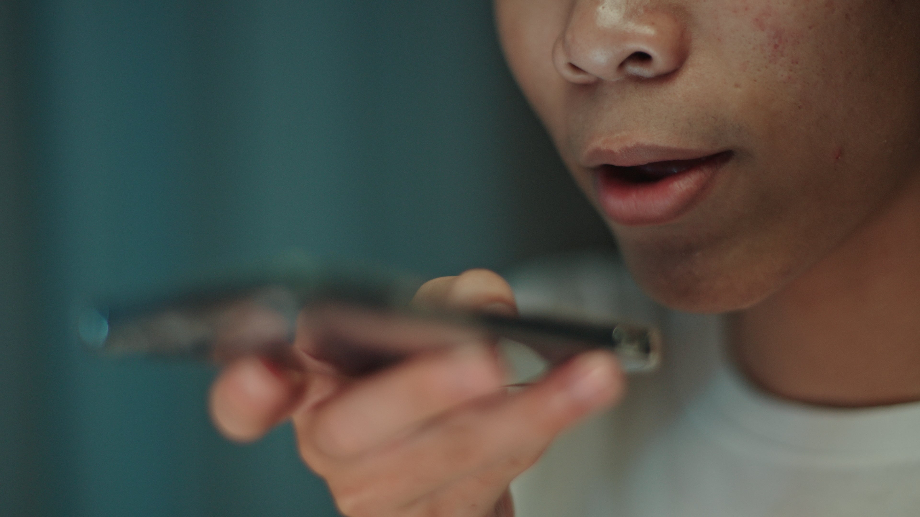 Person som holder en smarttelefon mot munnen, tilsynelatende snakker inn i den, med bare munnen og hånden synlig