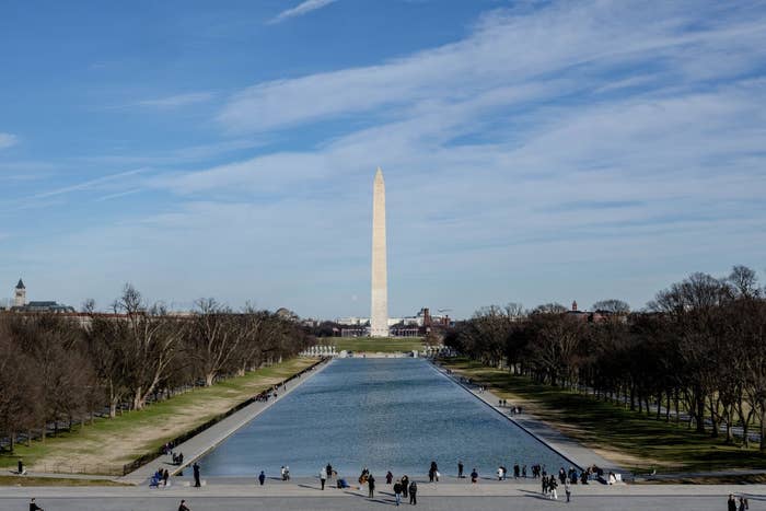 Washington Monument presumption    with Reflection Pool, radical   walking nearby. Clear sky, iconic American landmark setting