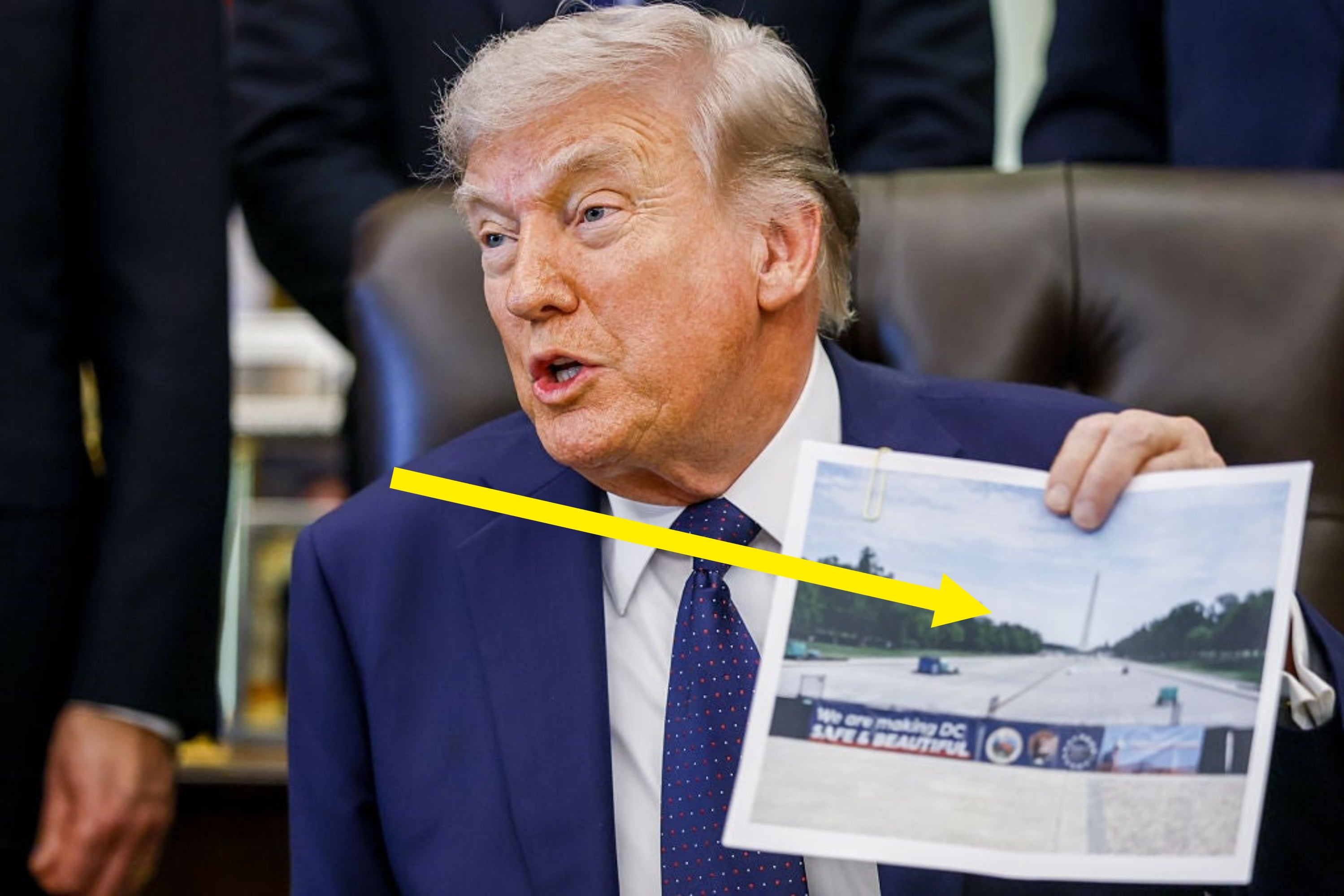 A person in a suit holds a printout of a photo while sitting at a desk