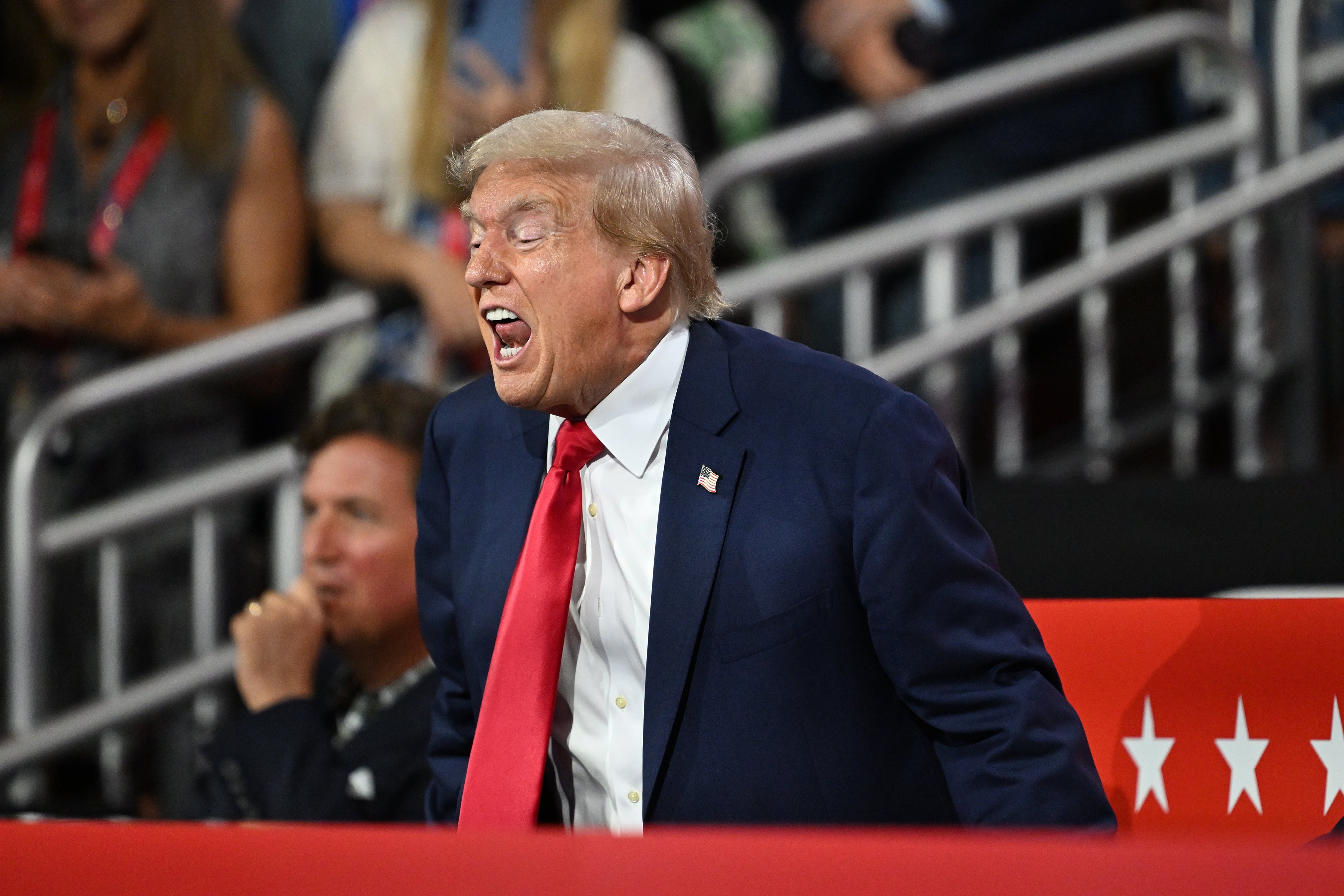 A man in a suit and red tie shouts passionately in an energetic public setting