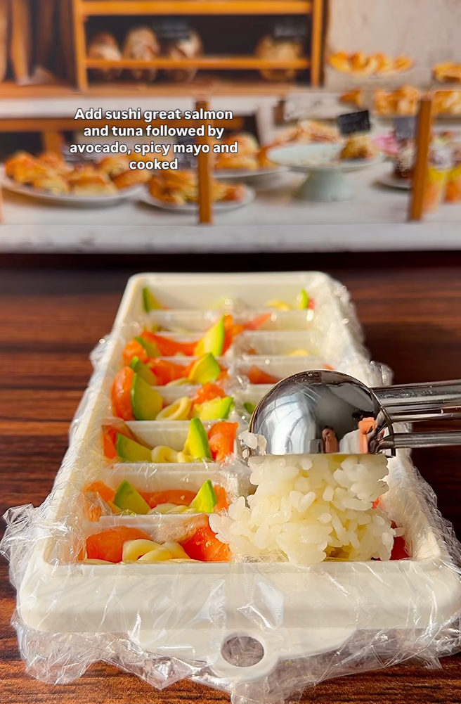 Tray of sushi rice being prepared with avocado and spicy mayo, following salmon and tuna