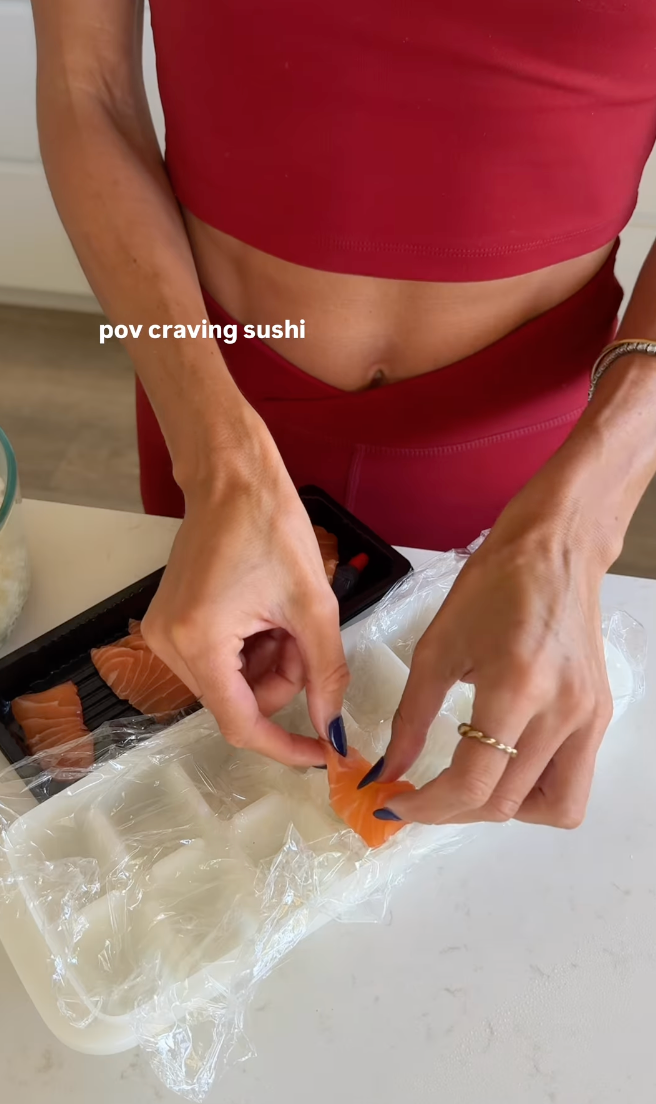 Person in athletic wear preparing sushi, placing salmon on rice. Text reads: "pov craving sushi."