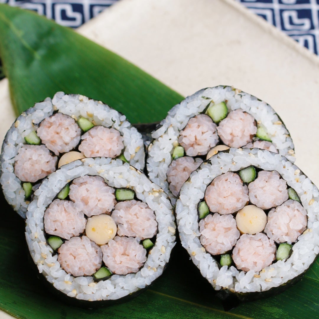 Sushi rolls shaped like flowers with rice, cucumber, and filling, arranged on a leaf