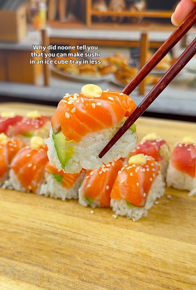 Chopsticks hold salmon-topped sushi with sesame seeds. Text suggests using an ice cube tray for sushi
