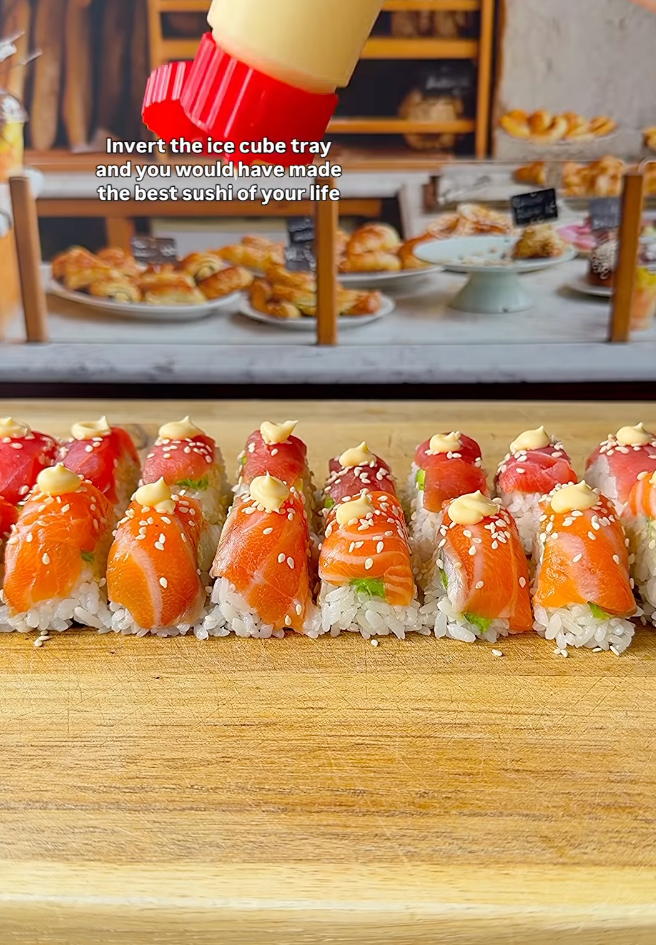 Sushi rolls topped with salmon and sesame seeds on a wooden board, with sauce being squeezed from a bottle. Text suggests using an ice cube tray