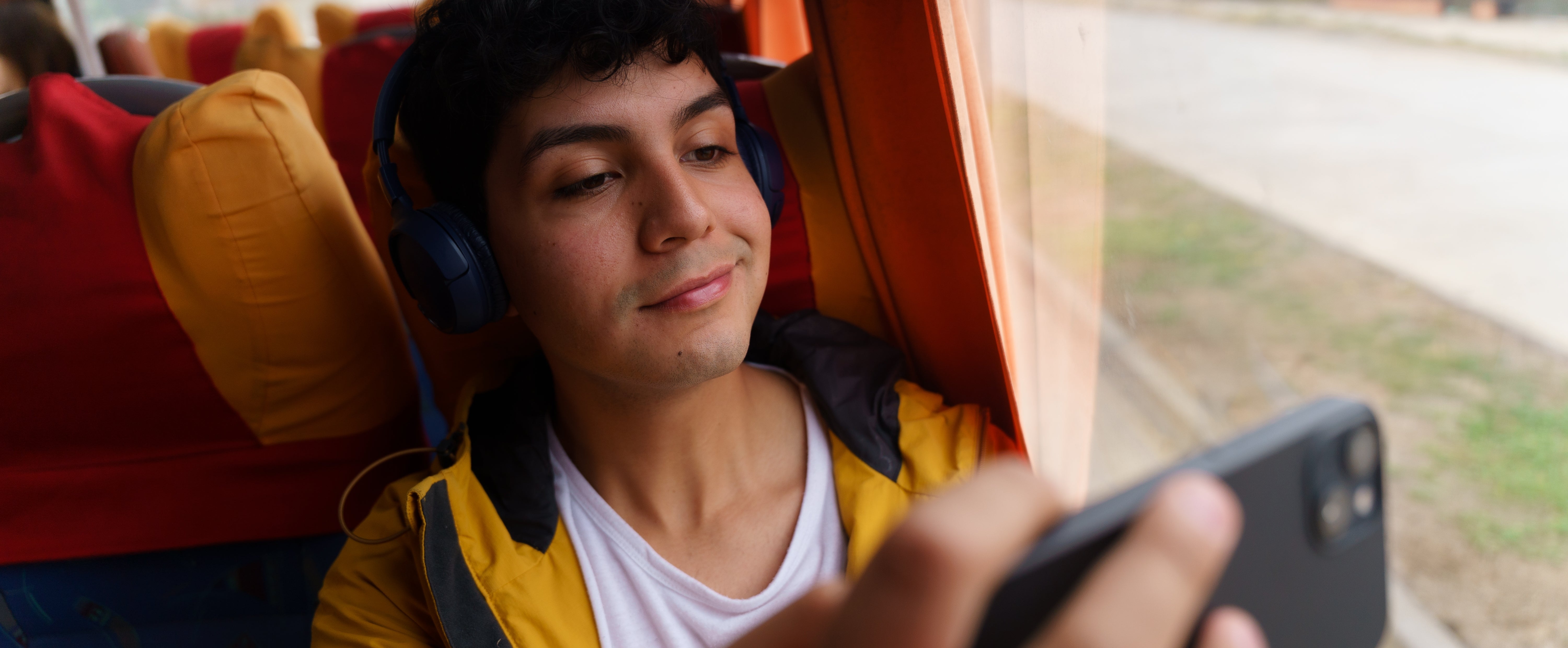 Person listening to headphones, smiling, and taking a selfie portion    sitting connected  a bus