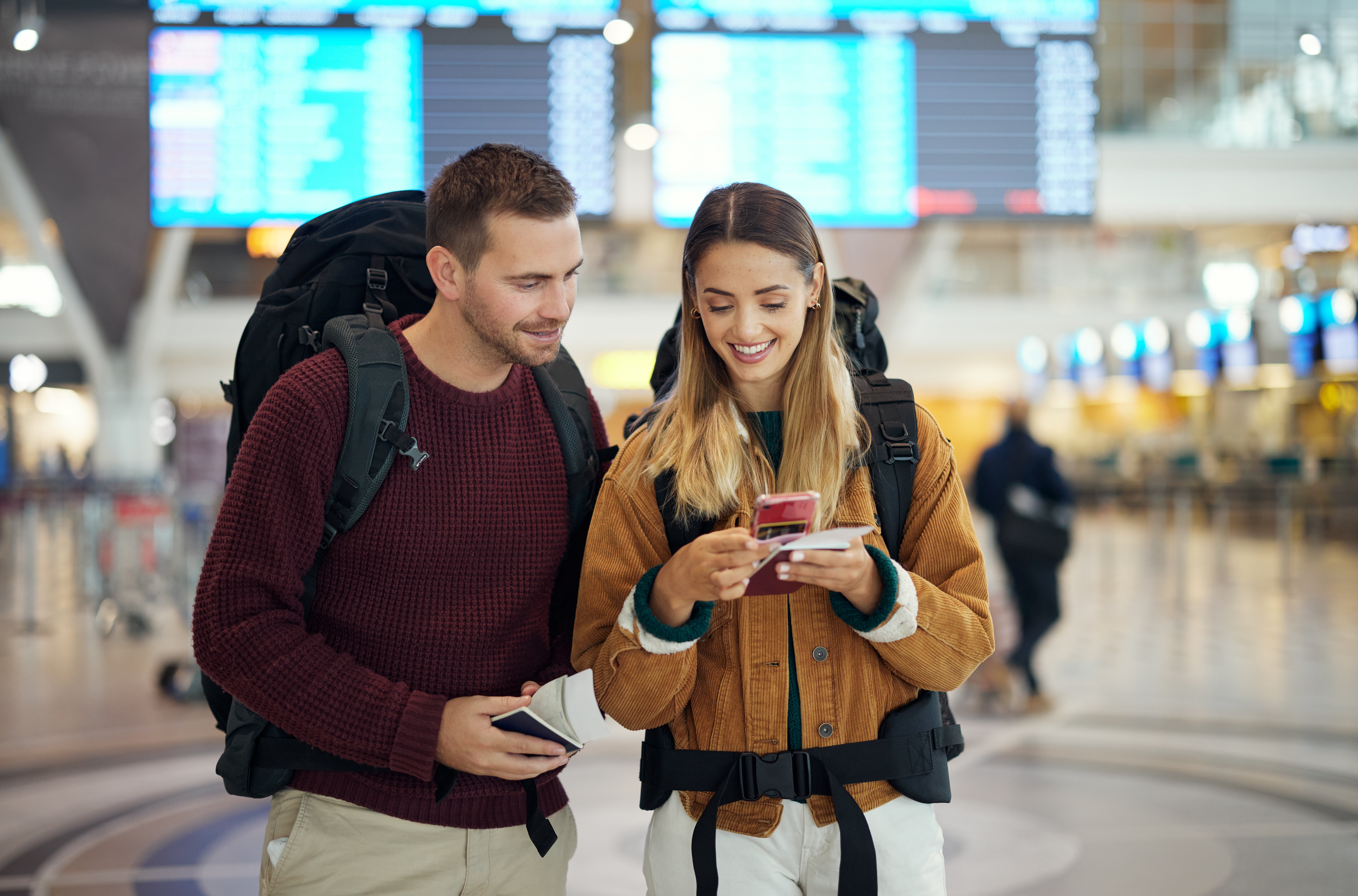 Two travelers with backpacks look   astatine  a telephone  unneurotic  successful  an airport, lasting  successful  beforehand   of a departures board