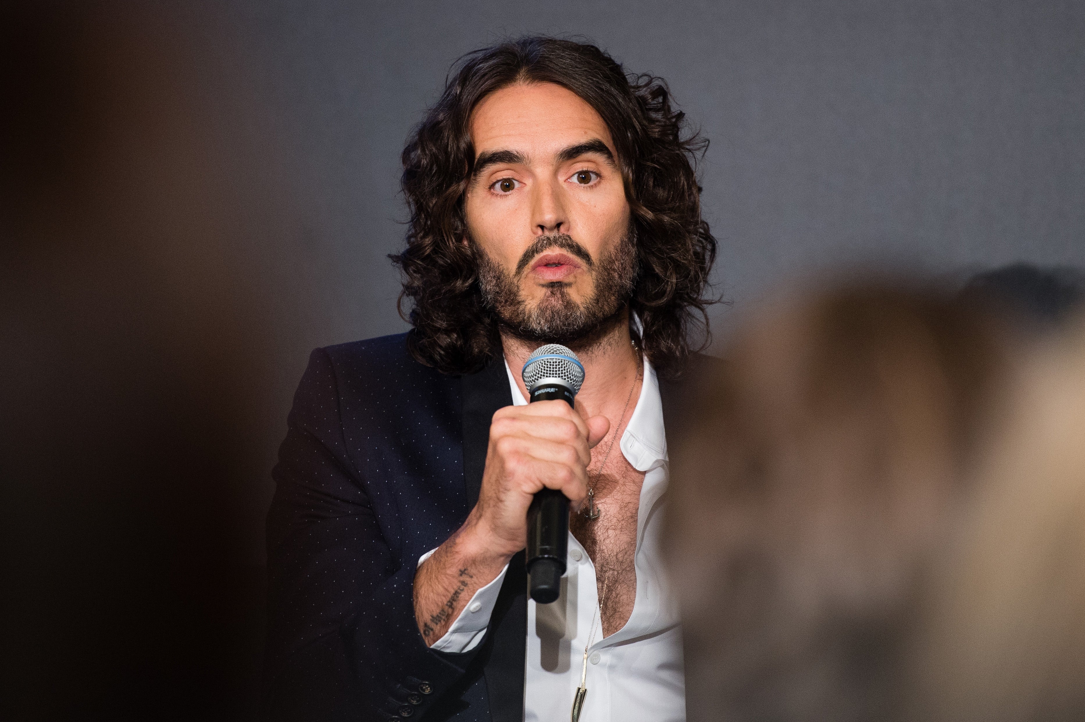 Russell Brand with agelong  hairsbreadth  successful  a blazer speaks into a microphone against a plain backdrop