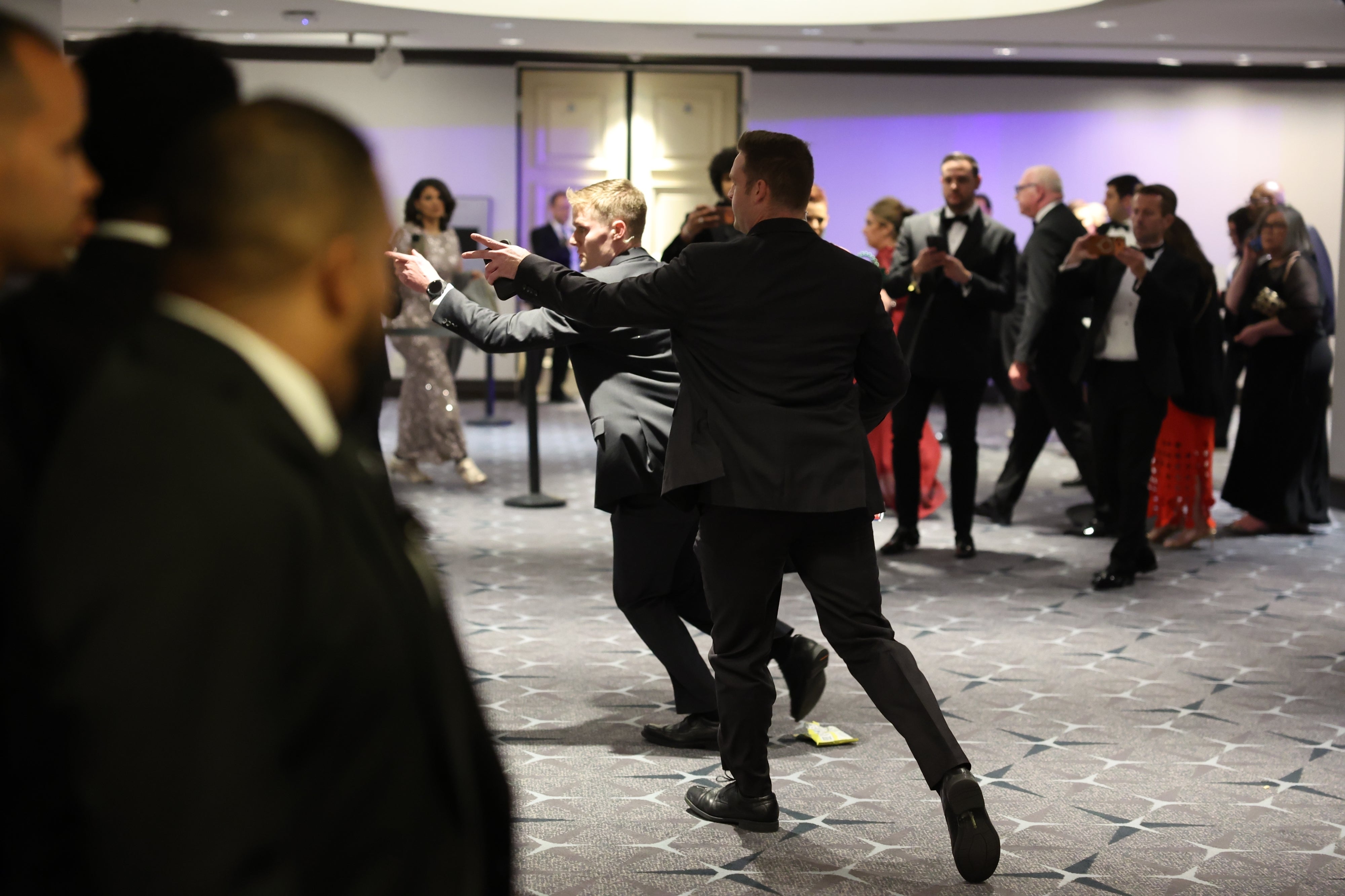 People in formal attire dance energetically at an indoor event, engaging with onlookers in a lively atmosphere