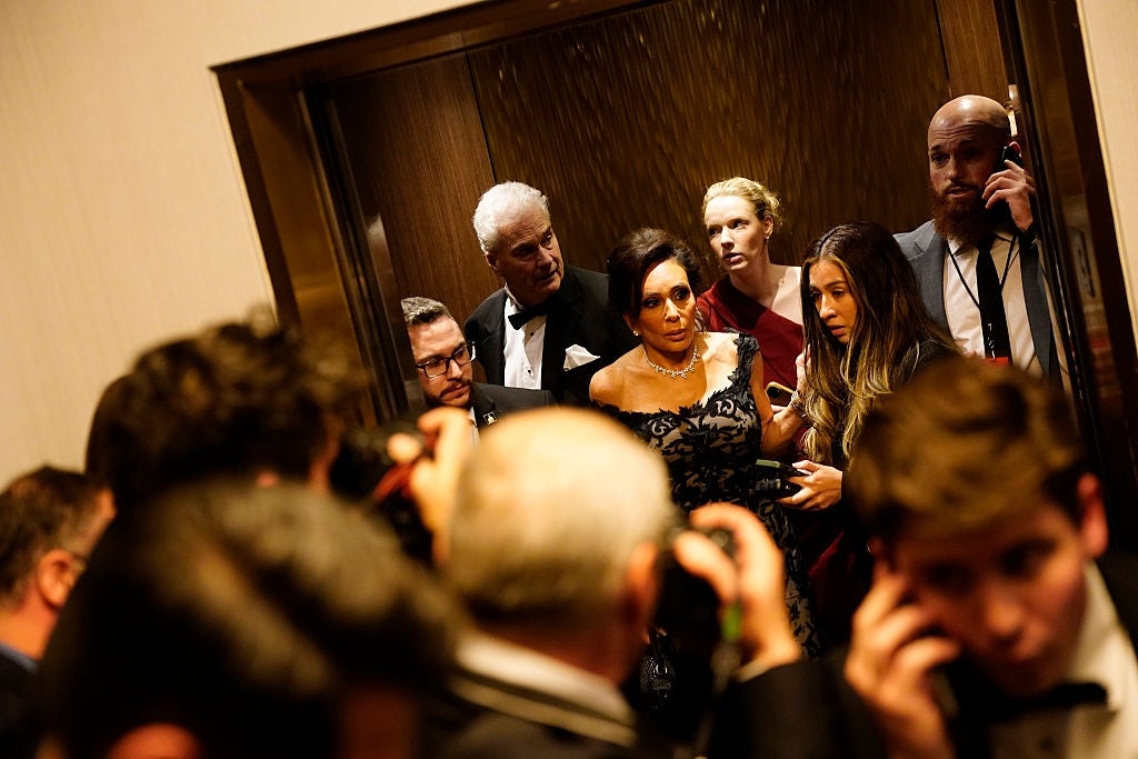 Group of elegantly dressed people in a crowded elevator, some using phones, during a formal event