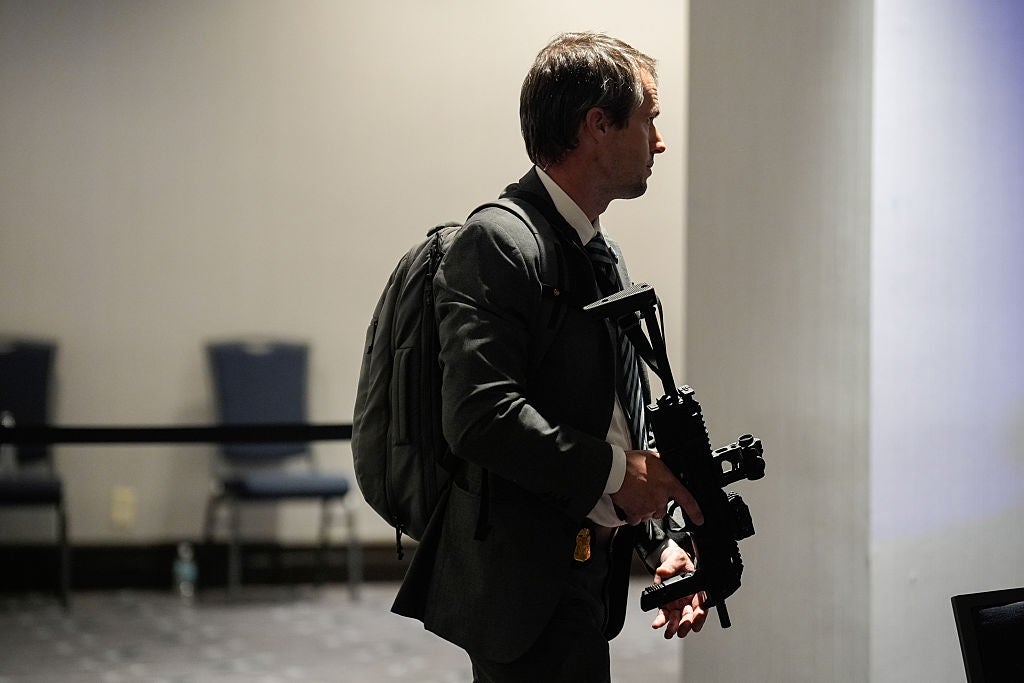 Person in a suit with a backpack holding camera equipment, in a conference setting