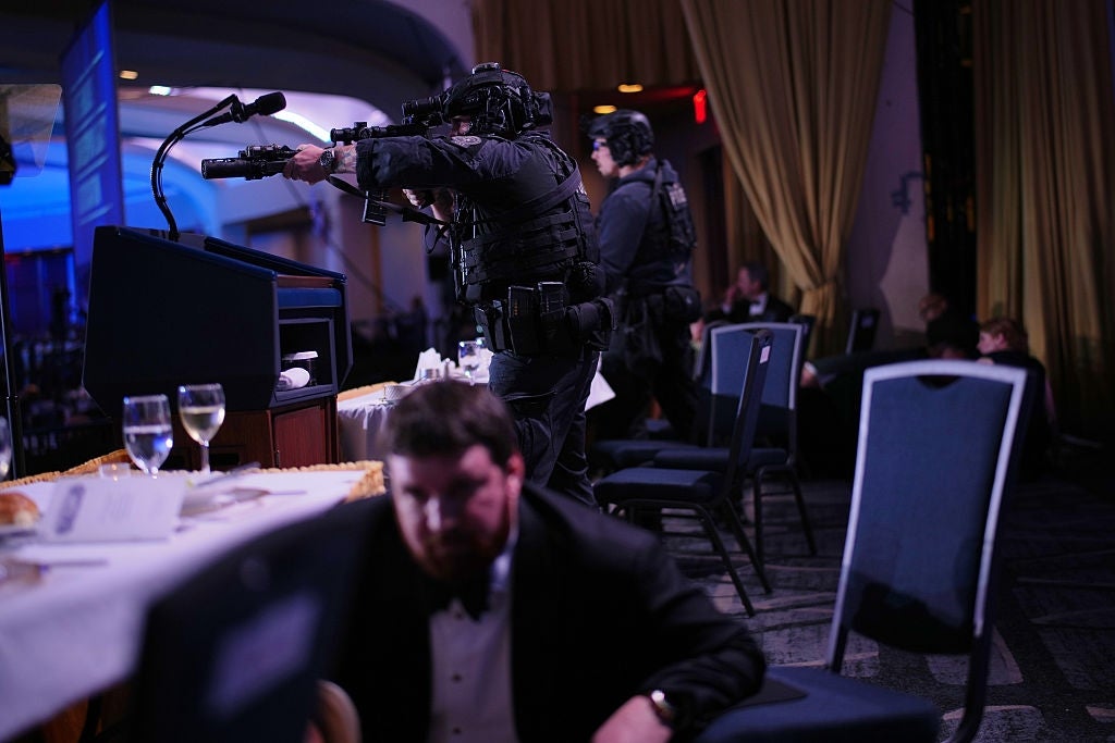 A SWAT team with rifles enters a formal event, with a man in a tuxedo taking cover under the table