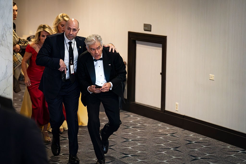 A man in a tuxedo is assisted by another man while descending a carpeted hallway, with people following behind them