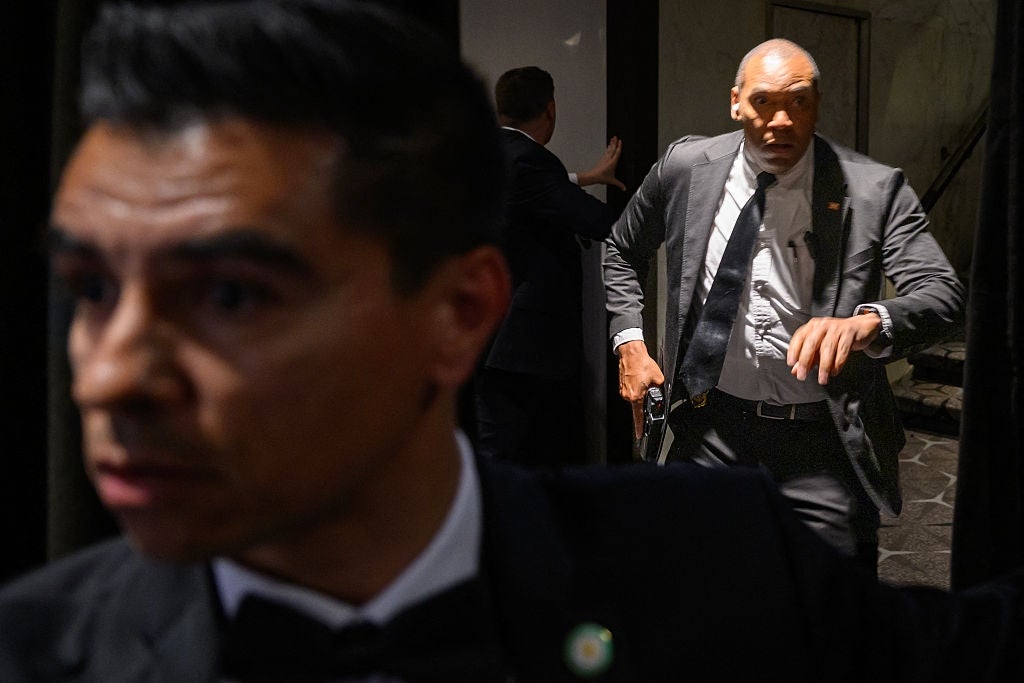 Two men in suits, possibly security personnel, looking alert. One is in the foreground, and the other holds a radio in the background