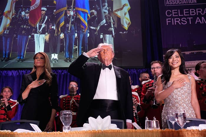 A formal event with guests saluting and posing; one man in a tuxedo between two women in elegant evening gowns
