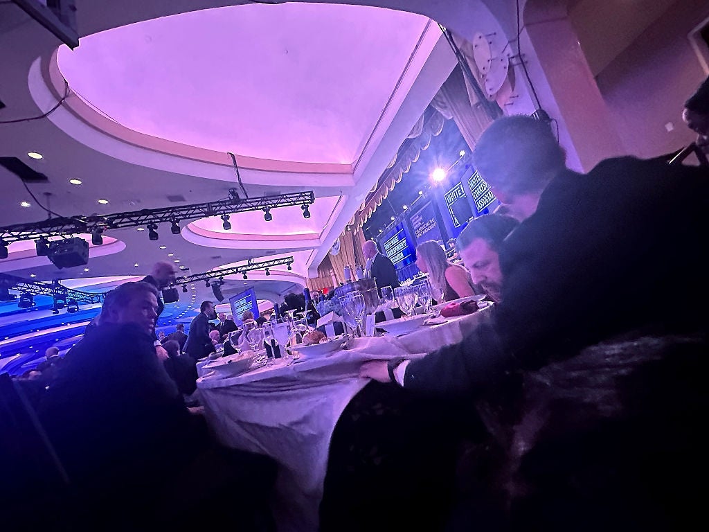 A formal event with attendees seated at tables in a large venue; a stage with displays is visible