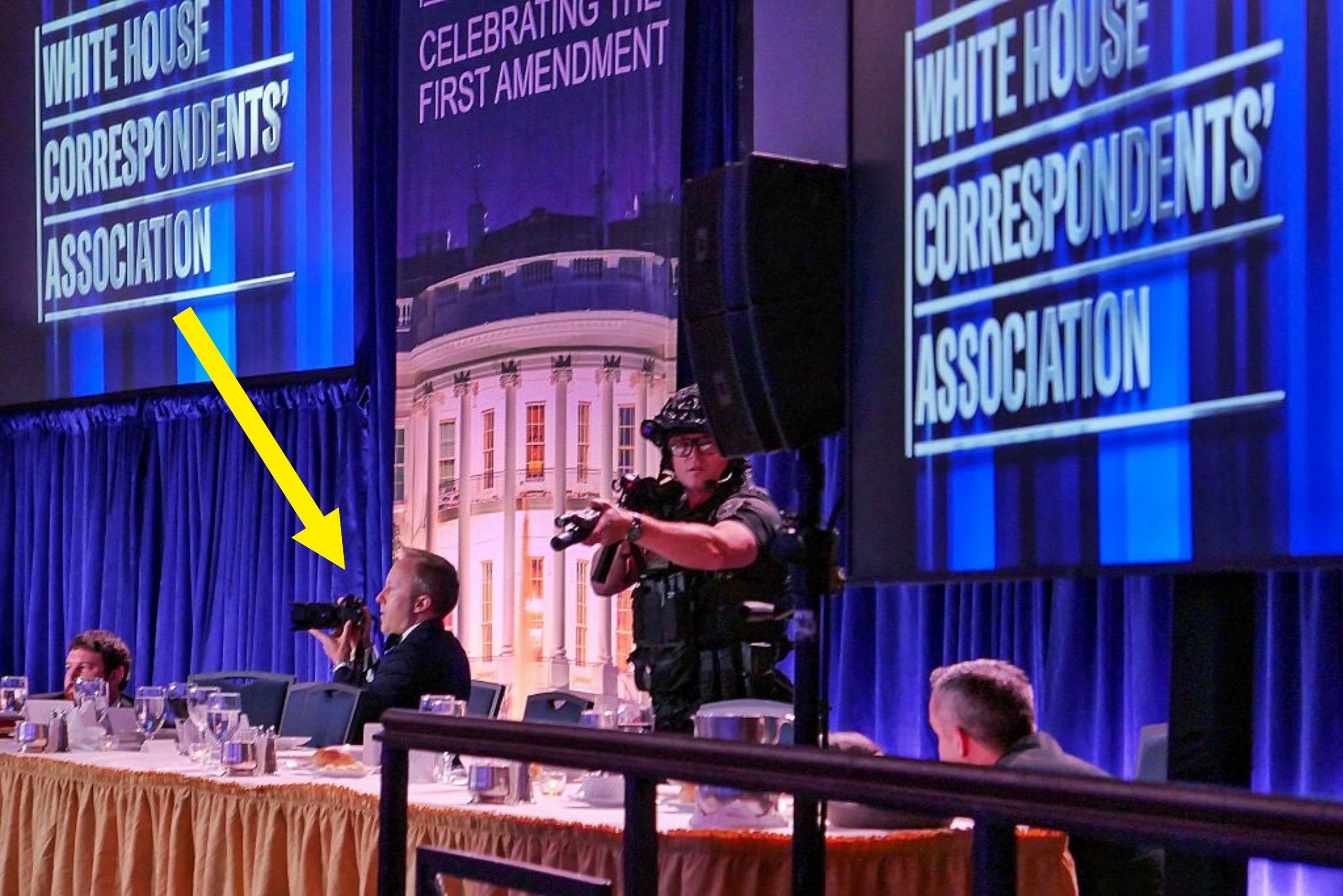 White House Correspondents' Dinner event with security personnel and attendees seated at tables. Large screens display event name