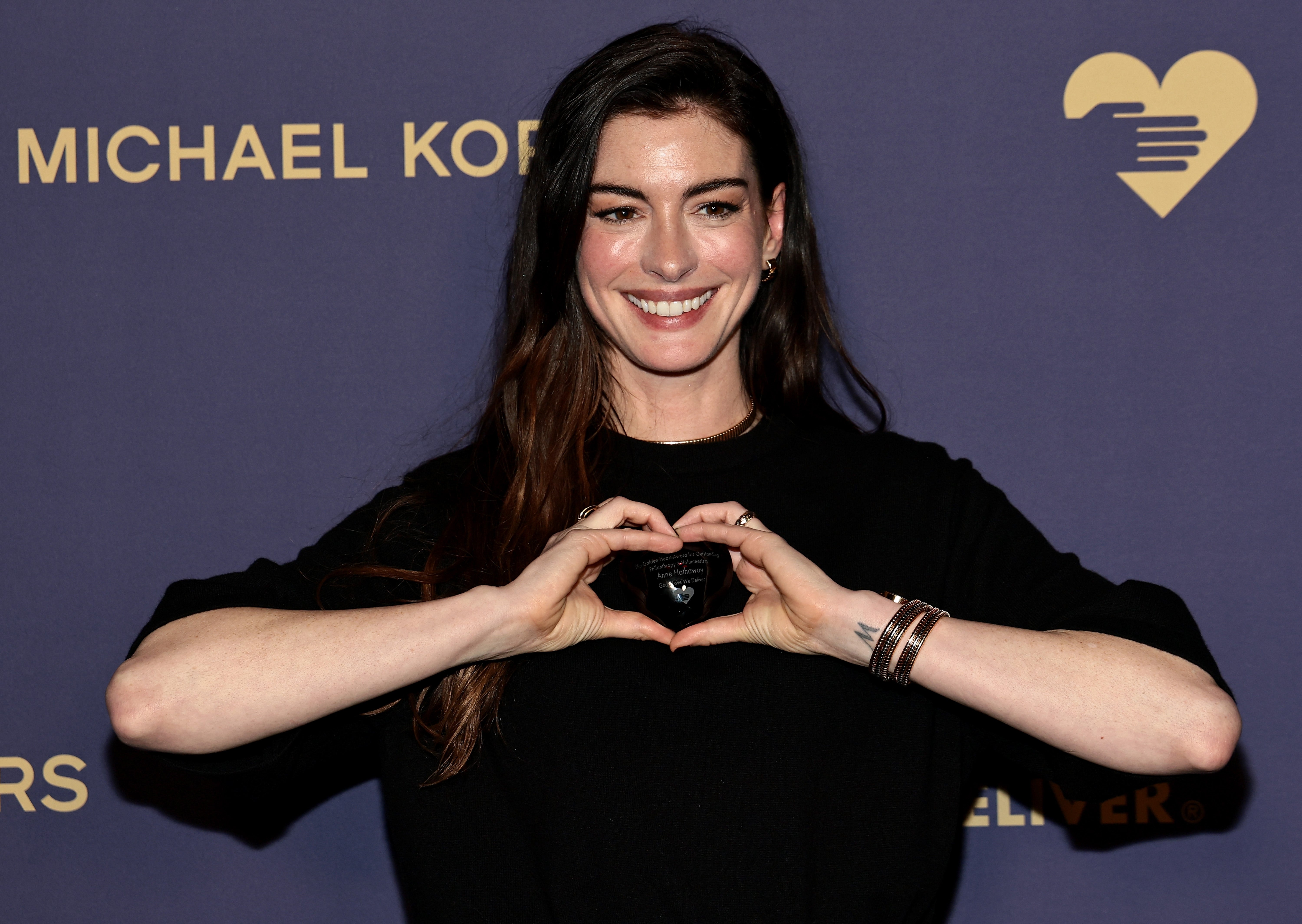 Anne Hathaway smiling, wearing a sweater, making a bosom  signifier   with hands astatine  a Michael Kors event