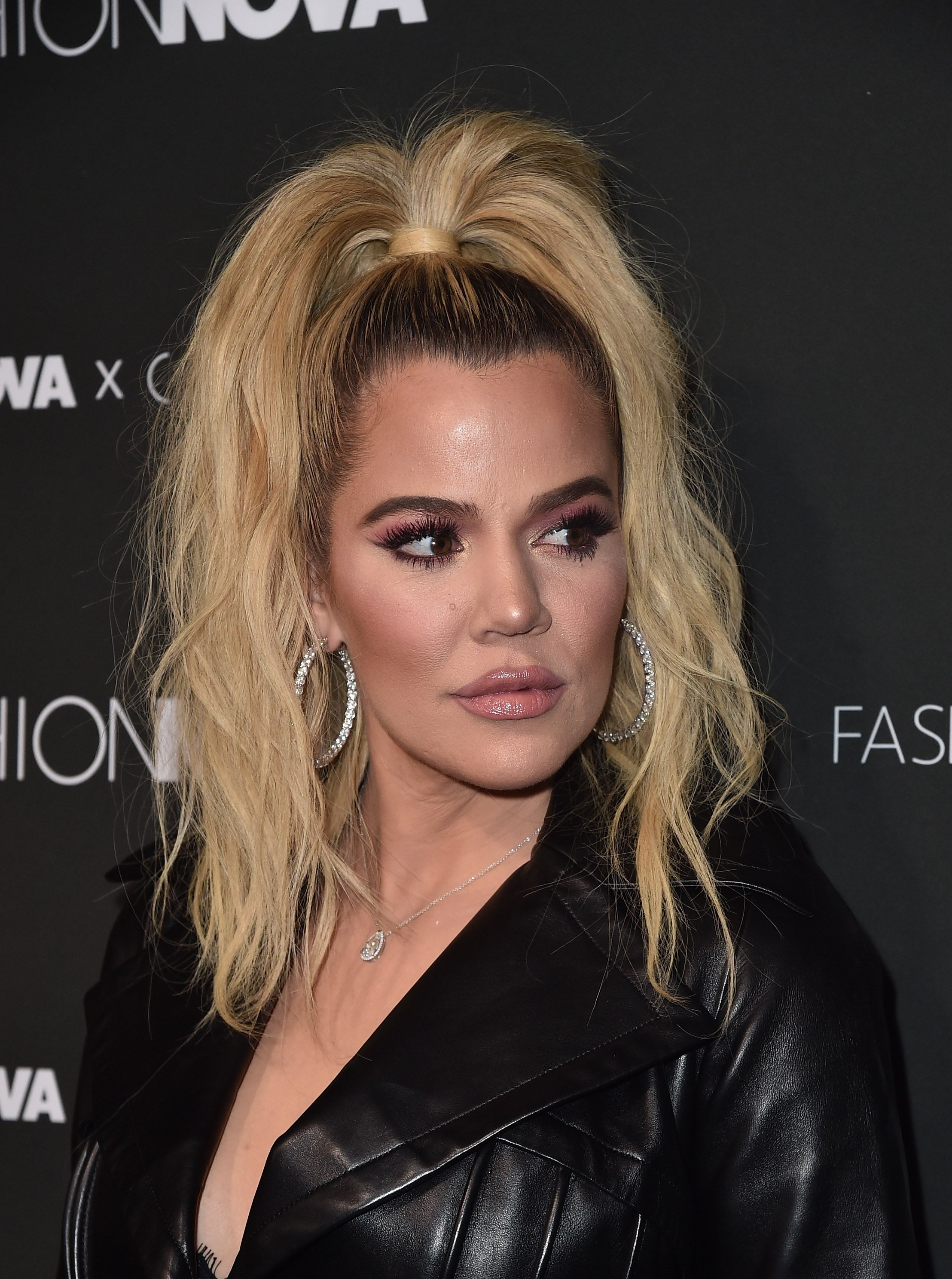 Khloe Kardashian with precocious   ponytail, hoop earrings, and a leather overgarment   poses astatine  a Fashion Nova event, looking to the side