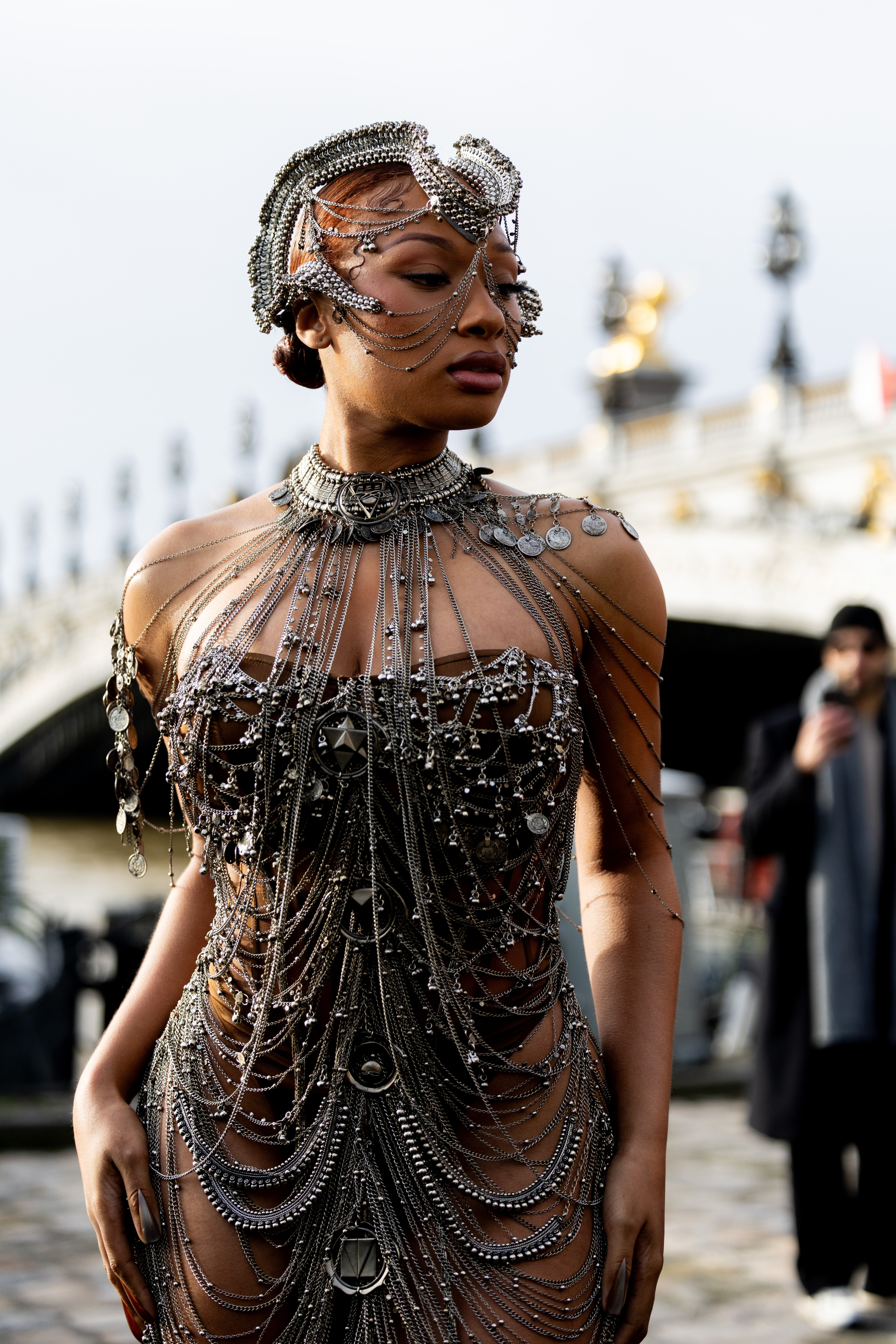 Megan Thee Stallion successful  an elaborate metallic outfit with layered chains and headpiece, posing outdoors astatine  an event, with a span  successful  the background