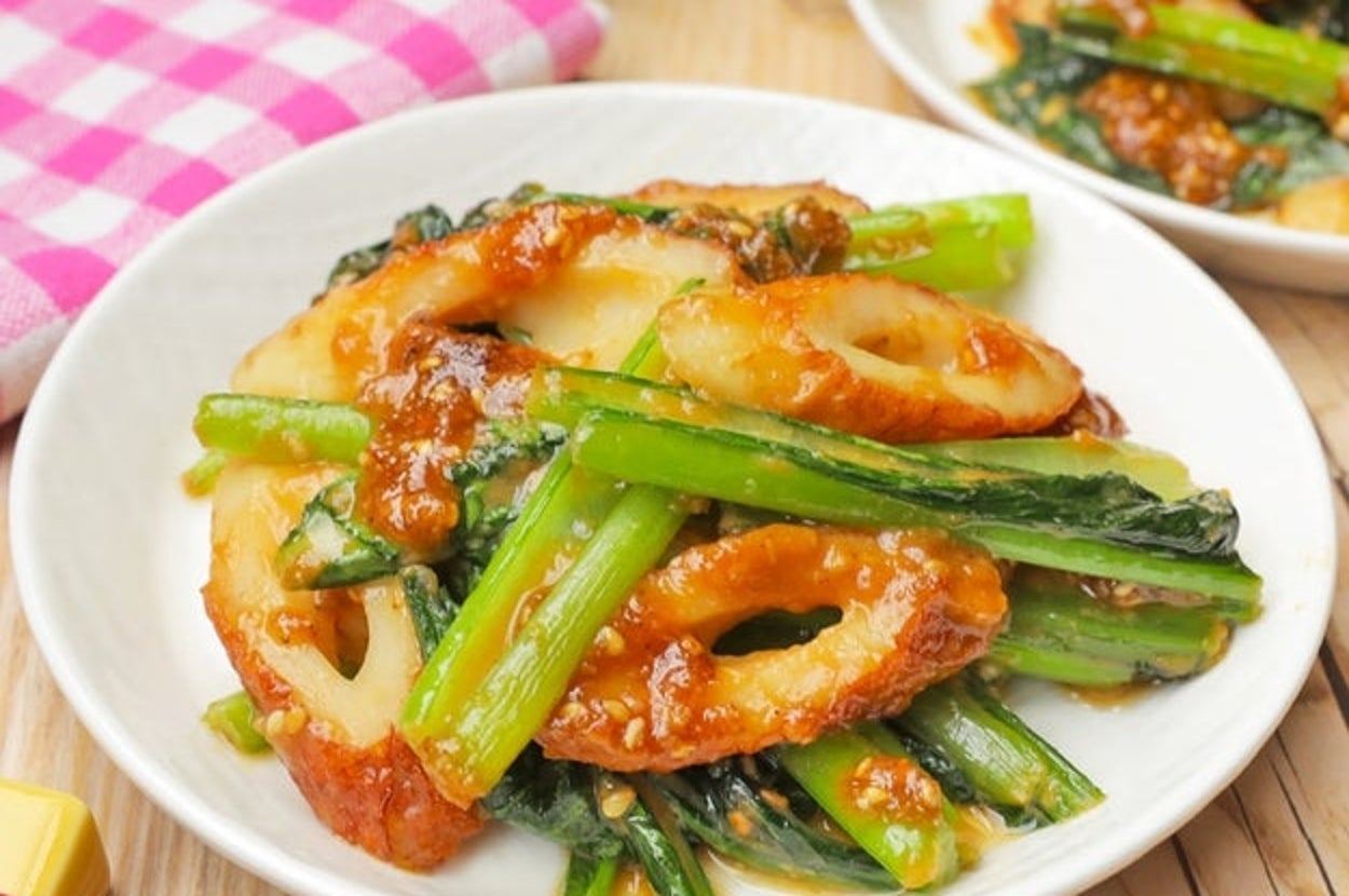 白い皿に盛られたちくわと青菜の炒め物。赤い箸が添えられている。