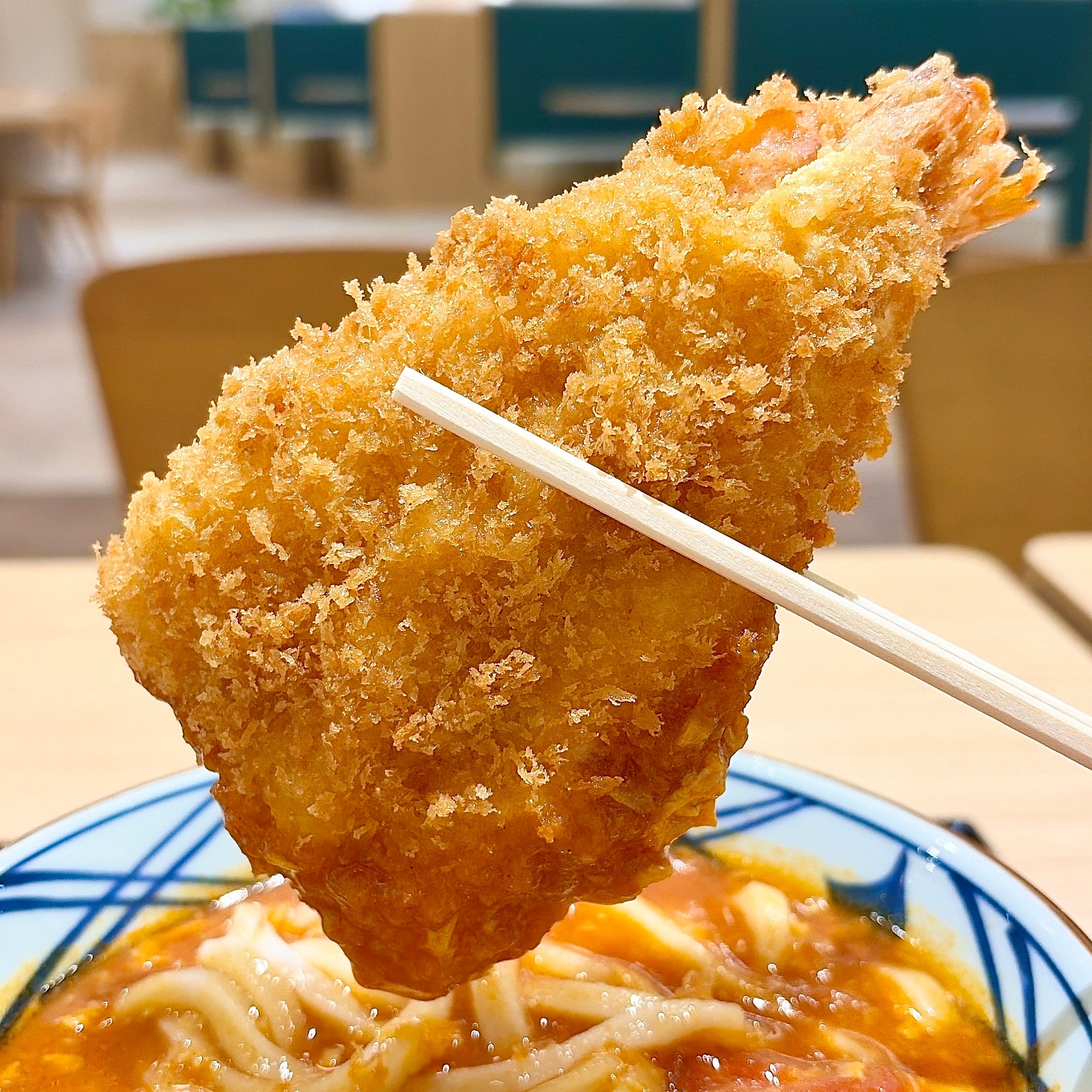 丸亀製麺「海老カツトマたまカレーうどん」テーブルでエビをうどんの上に持ち上げた様子。食欲をそそる料理の一瞬。
