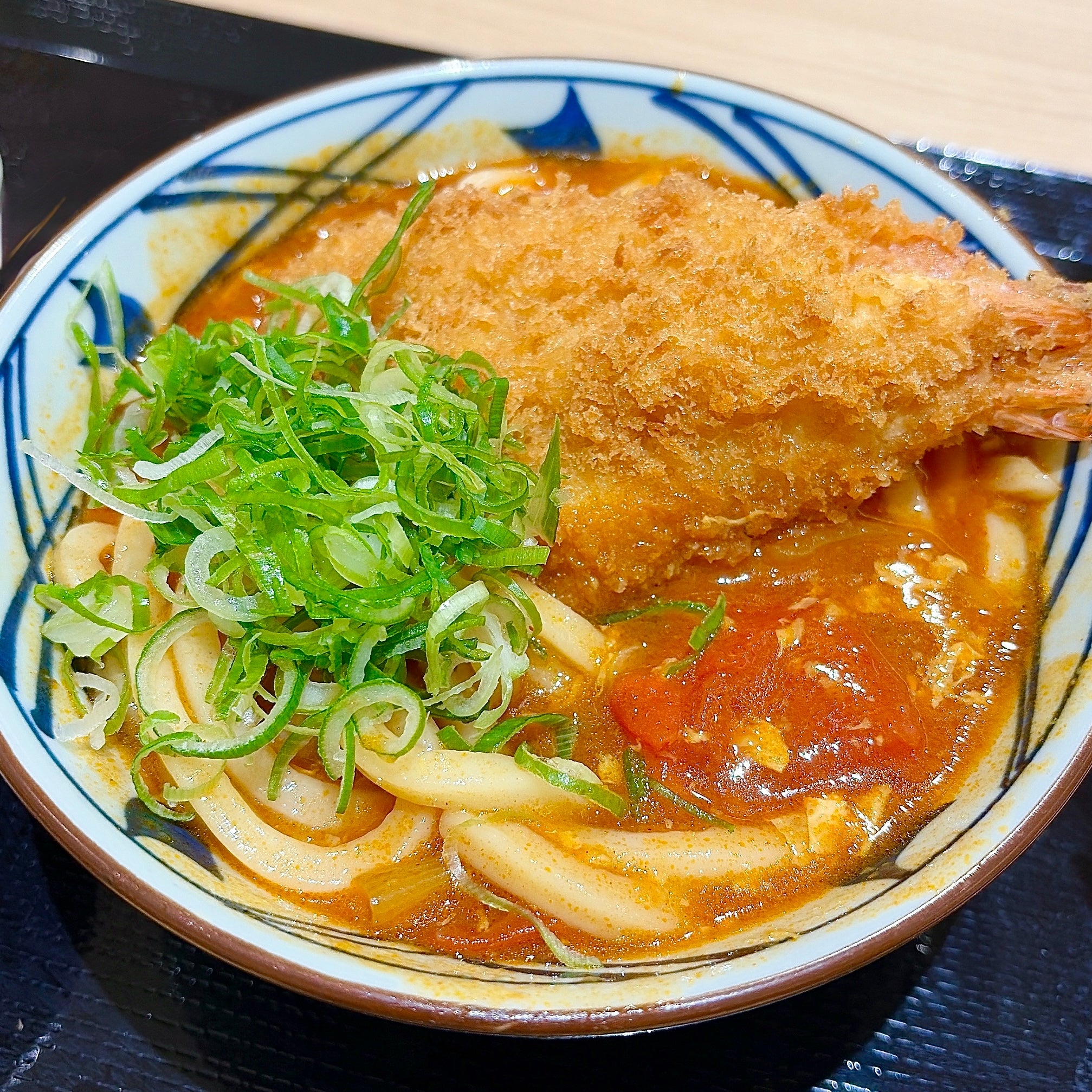 丸亀製麺「海老カツトマたまカレーうどん」カレーうどんにカツがトッピングされ、刻みネギが添えられた料理。