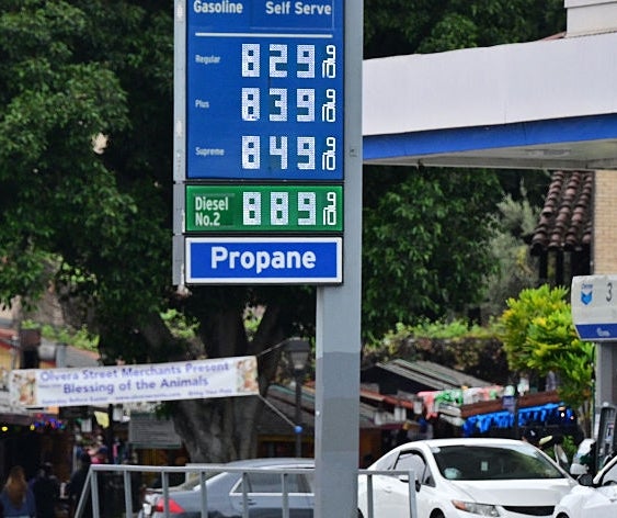 Bensinstasjonsskilt som viser priser: Vanlig $6,29, Midgrade $6,39, Premium $6,49, Diesel $6,59. Biler parkert i nærheten av food mart baldakin. Gatemarked i bakgrunnen