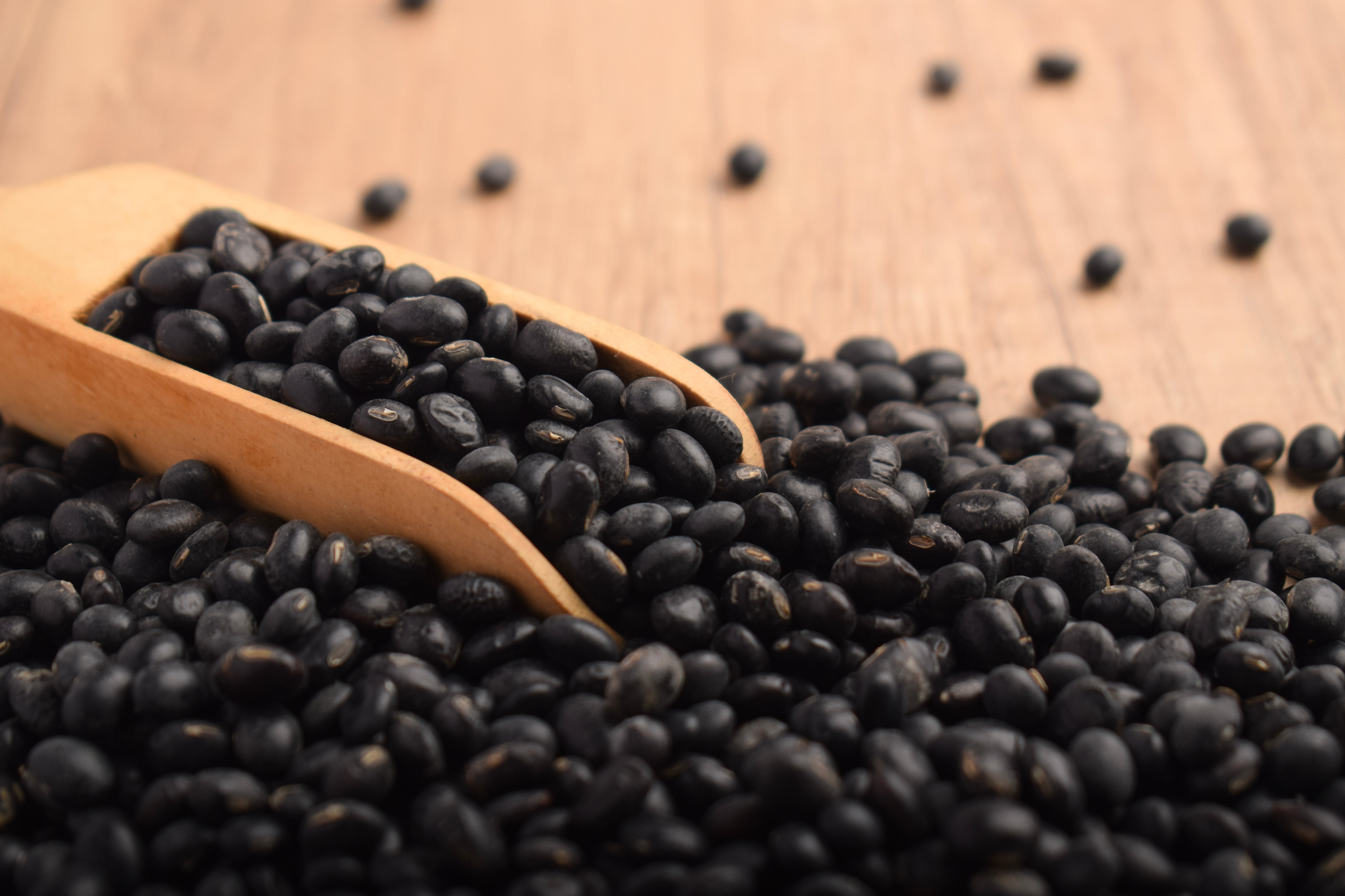 Wooden scoop with black beans spilling onto a wooden surface