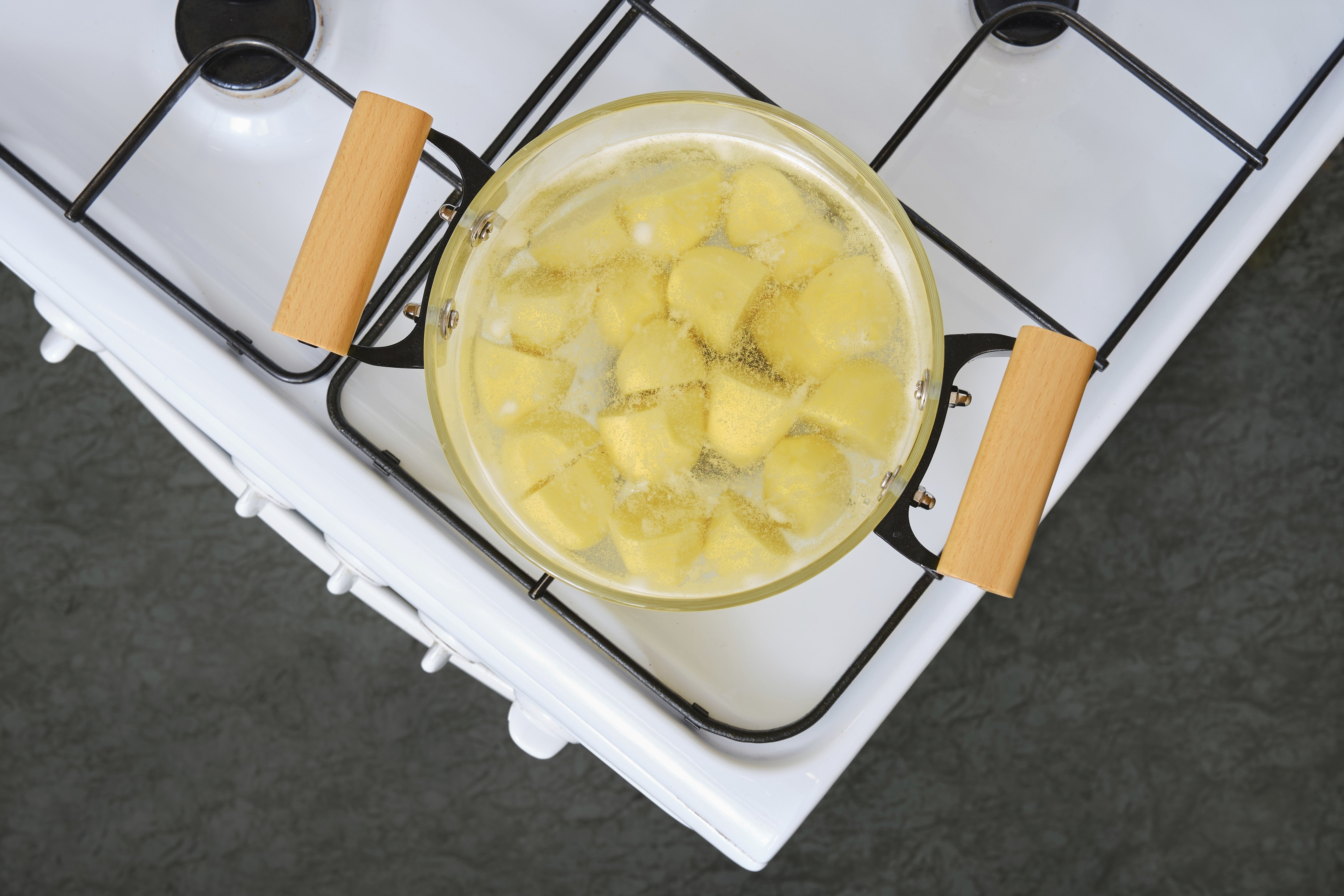 Pot with boiling water and yellow potatoes on a gas stove seen from above