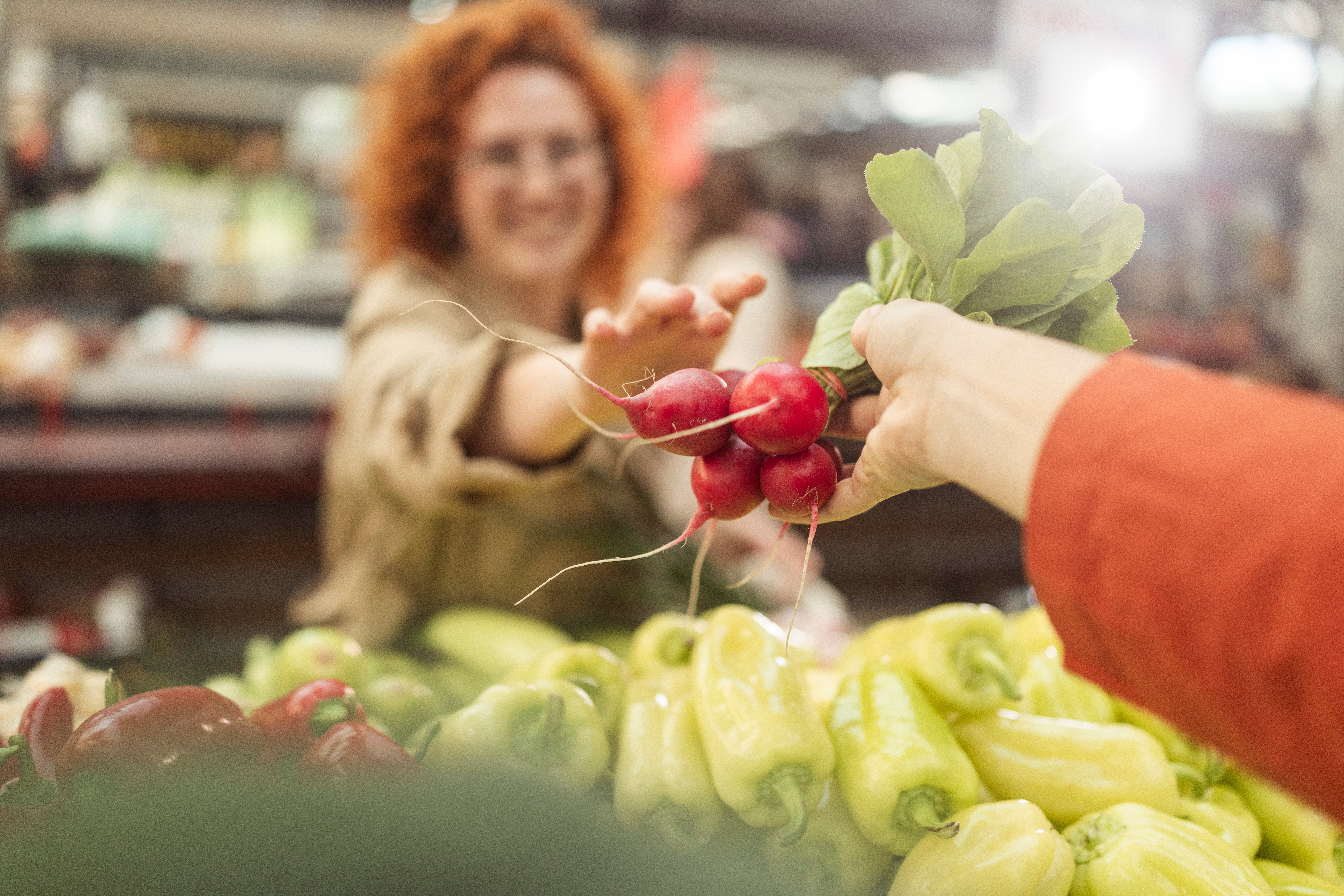 Person buying a bunch of radishes from a vendor at a market, with peppers visible in the foreground