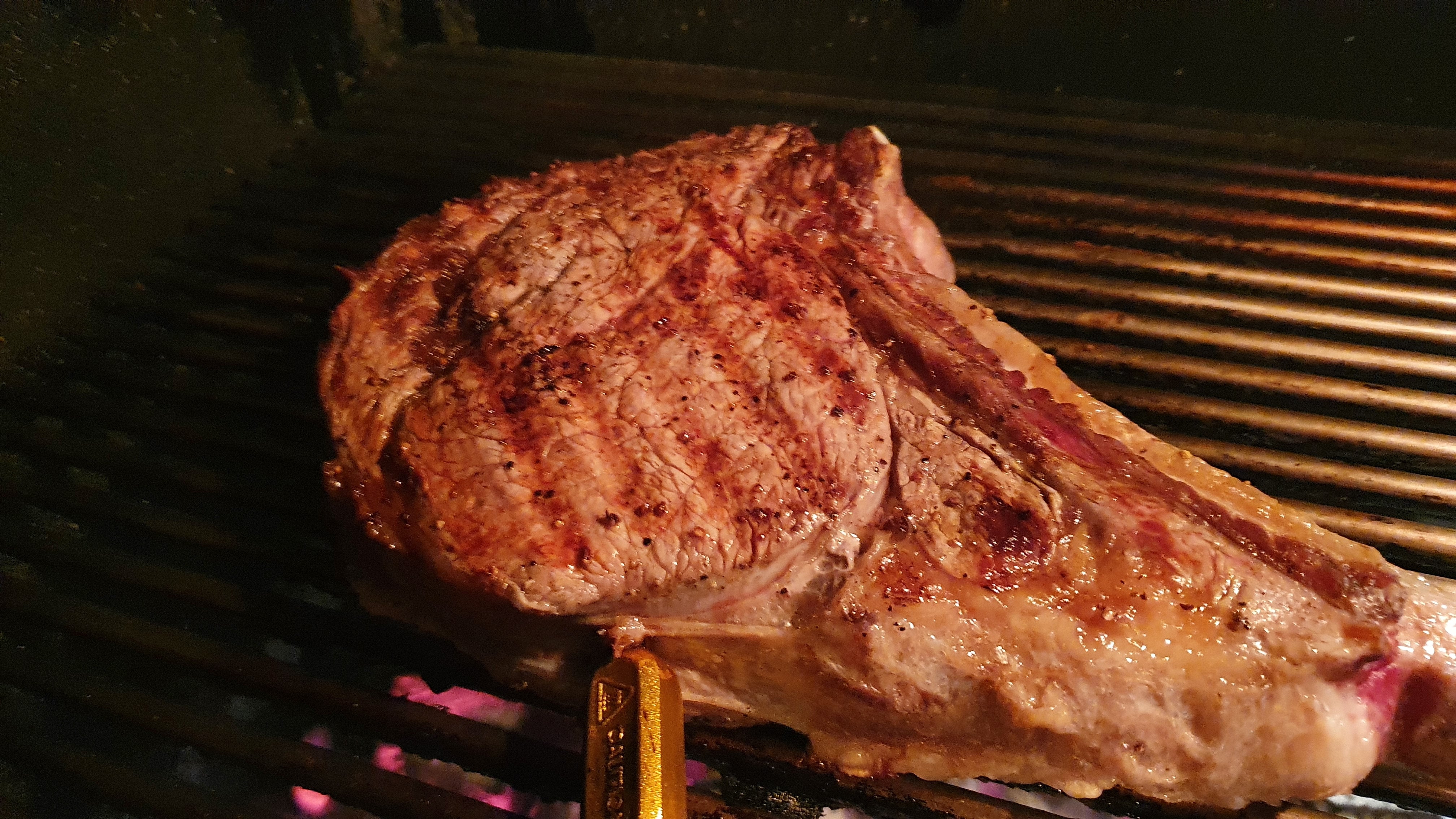 Steak cooking connected  a grill with a nutrient   thermometer inserted, showing grill marks