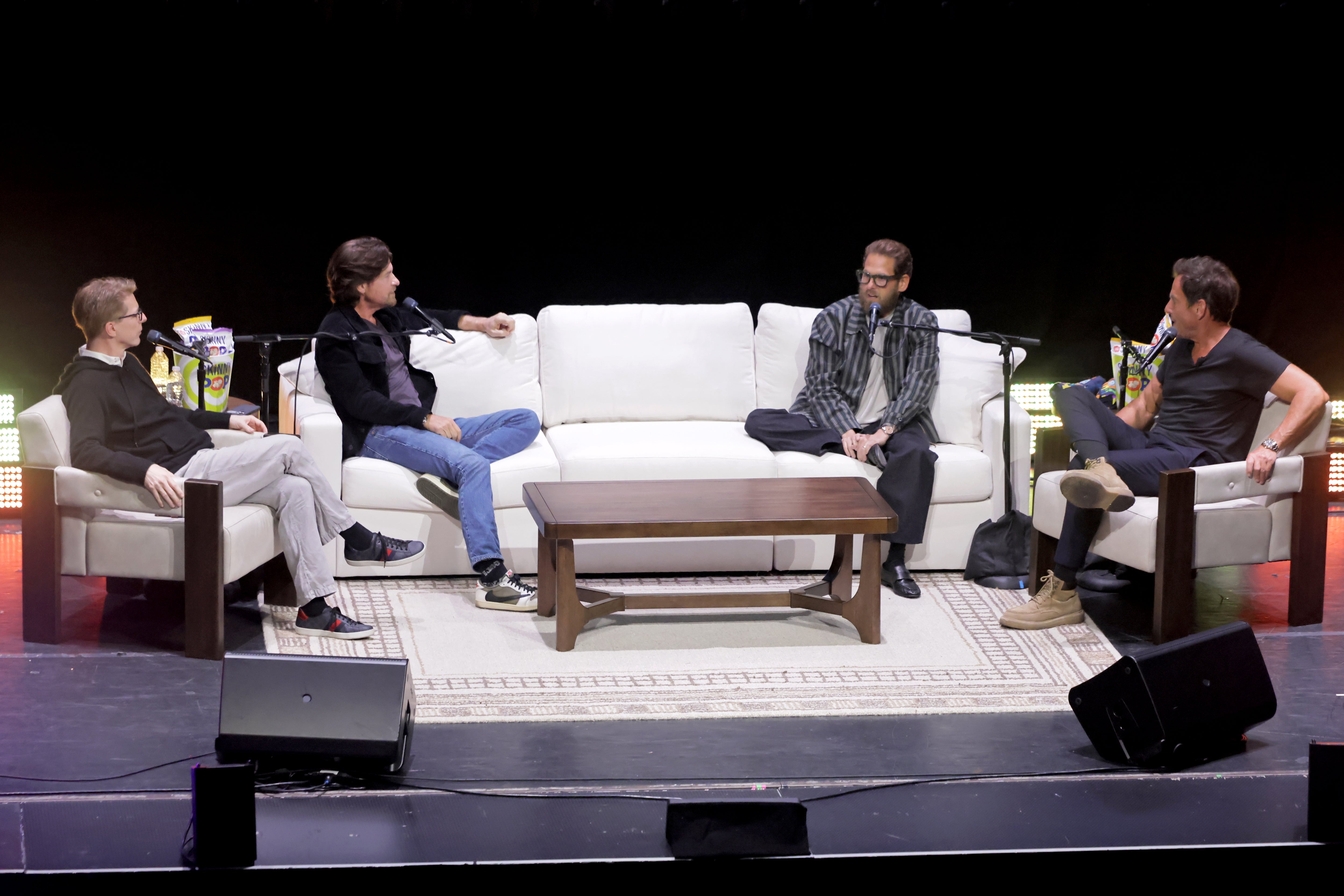 Four radical   successful  a sheet  treatment  connected  signifier    with microphones, seated connected  sofas astir   a java  table