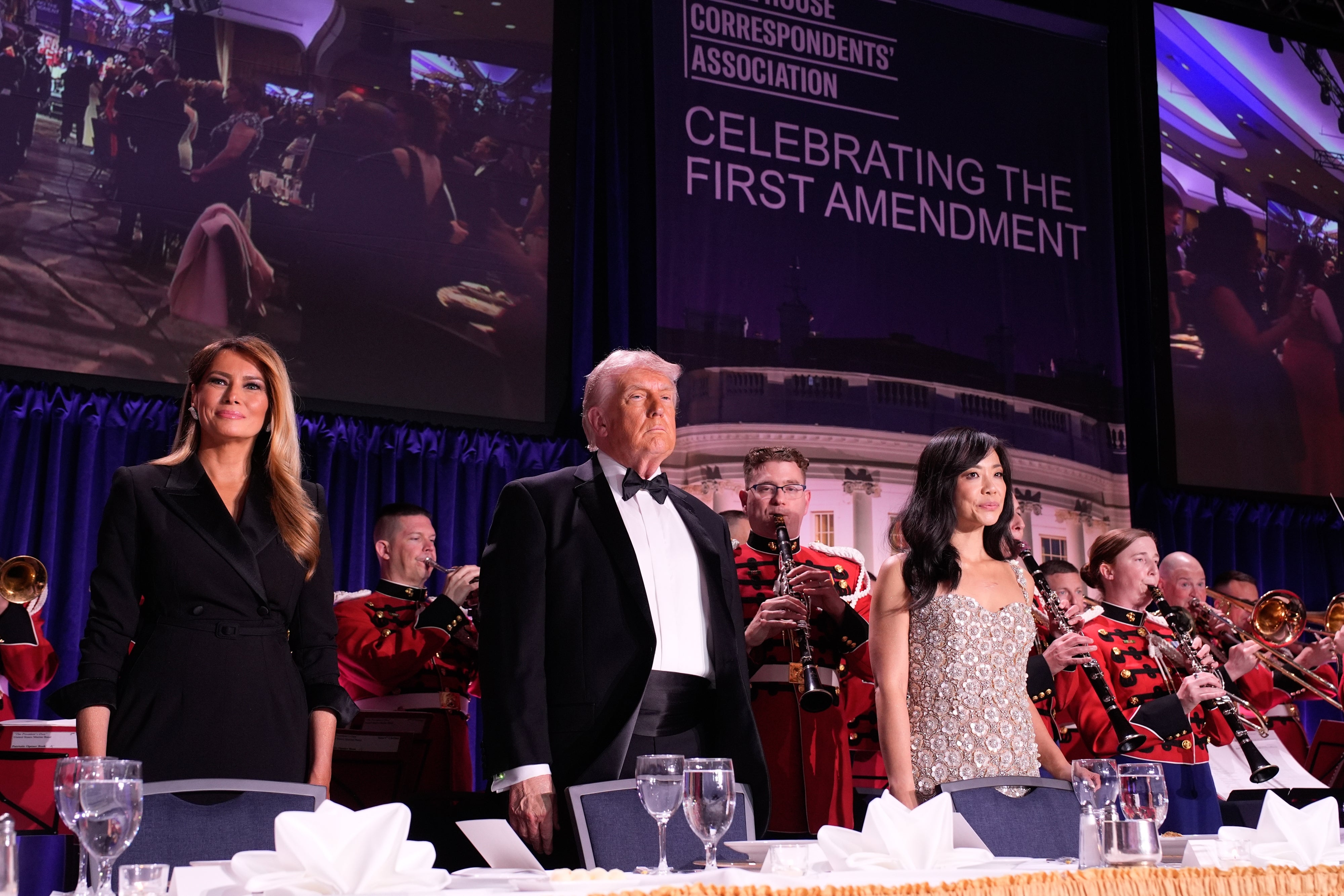 Three radical   basal   successful  ceremonial  attire astatine  a banquet, with a set  playing down  them. A ample  banner reads "Celebrating the First Amendment."