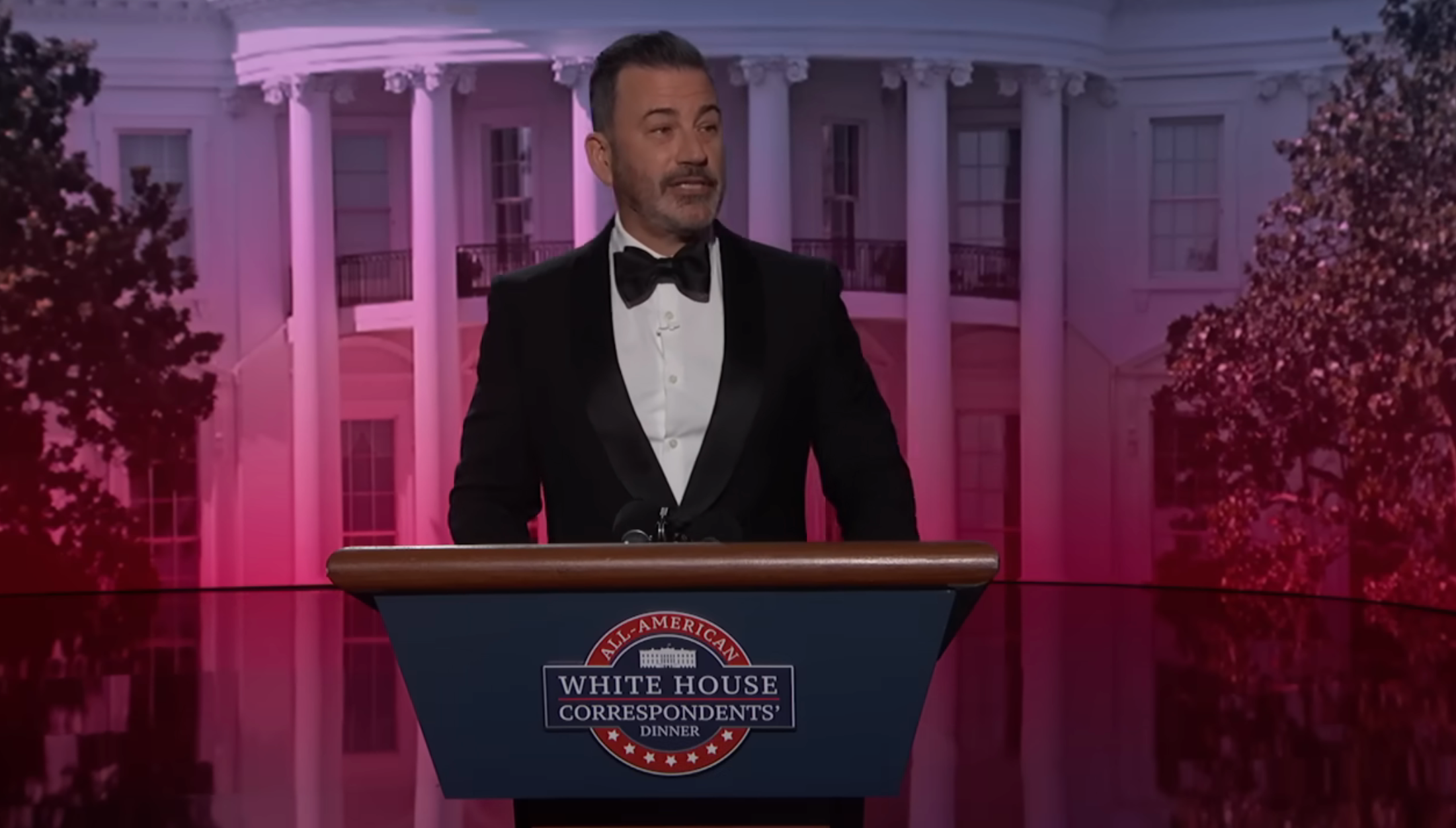 A idiosyncratic   successful  a tuxedo speaks astatine  a podium labeled "White House Correspondents' Dinner," with a gathering  backdrop