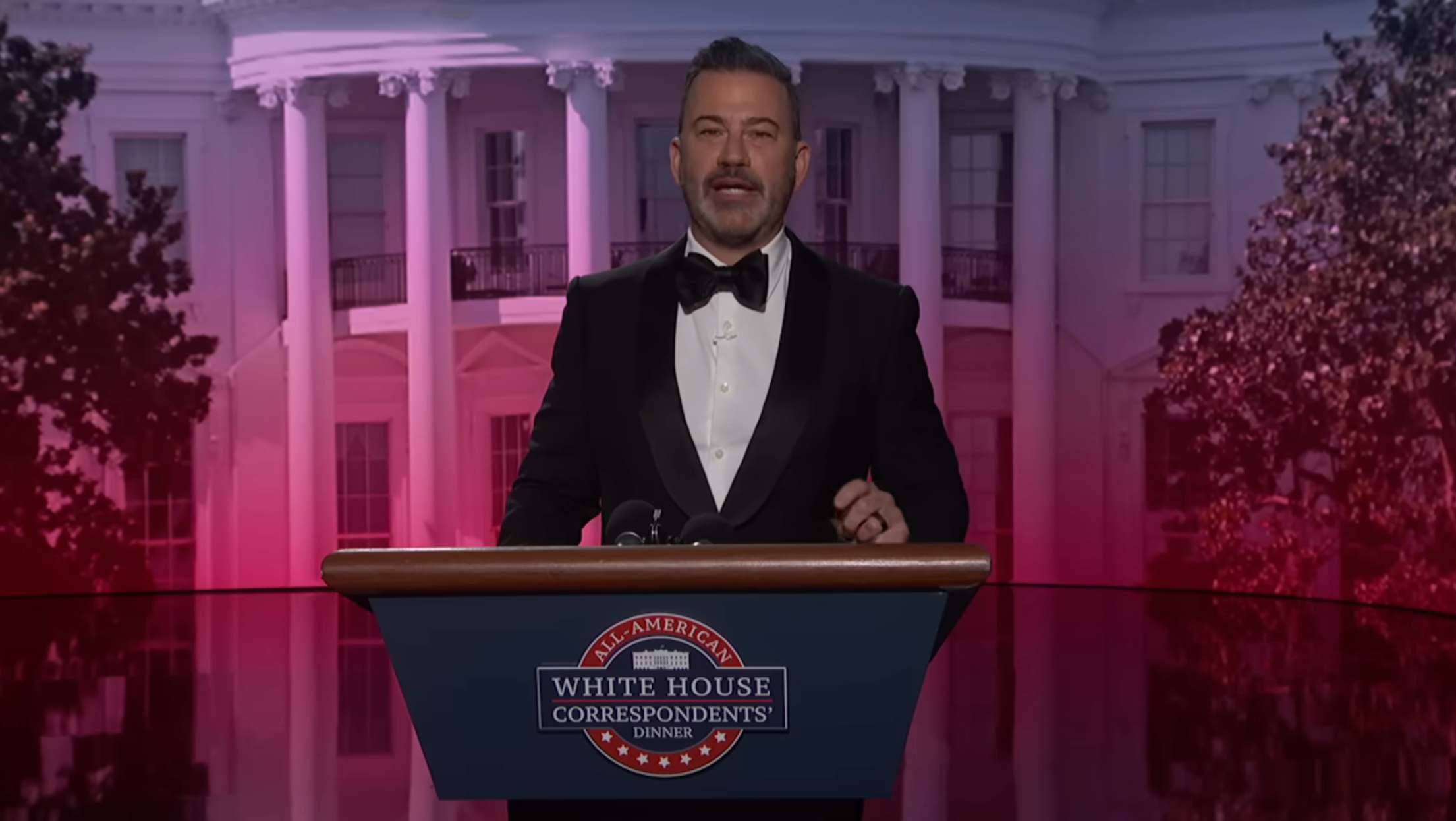 Man successful  a tuxedo speaking astatine  a podium labeled "White House Correspondents' Dinner," with a backdrop of the White House