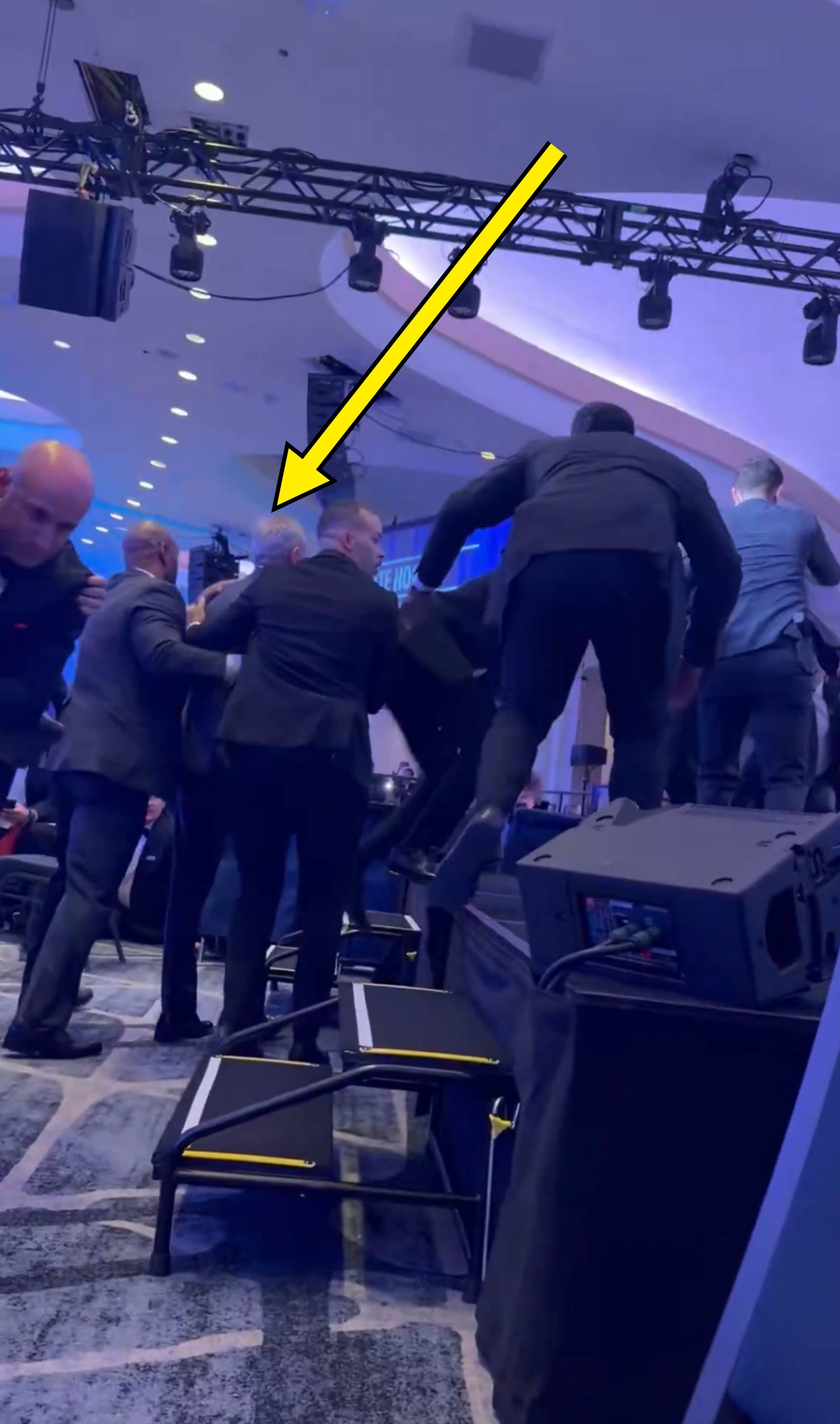 People successful  suits are successful  a chaotic country   connected  a stage, suggesting a imaginable  altercation oregon  scuffle astatine  an event