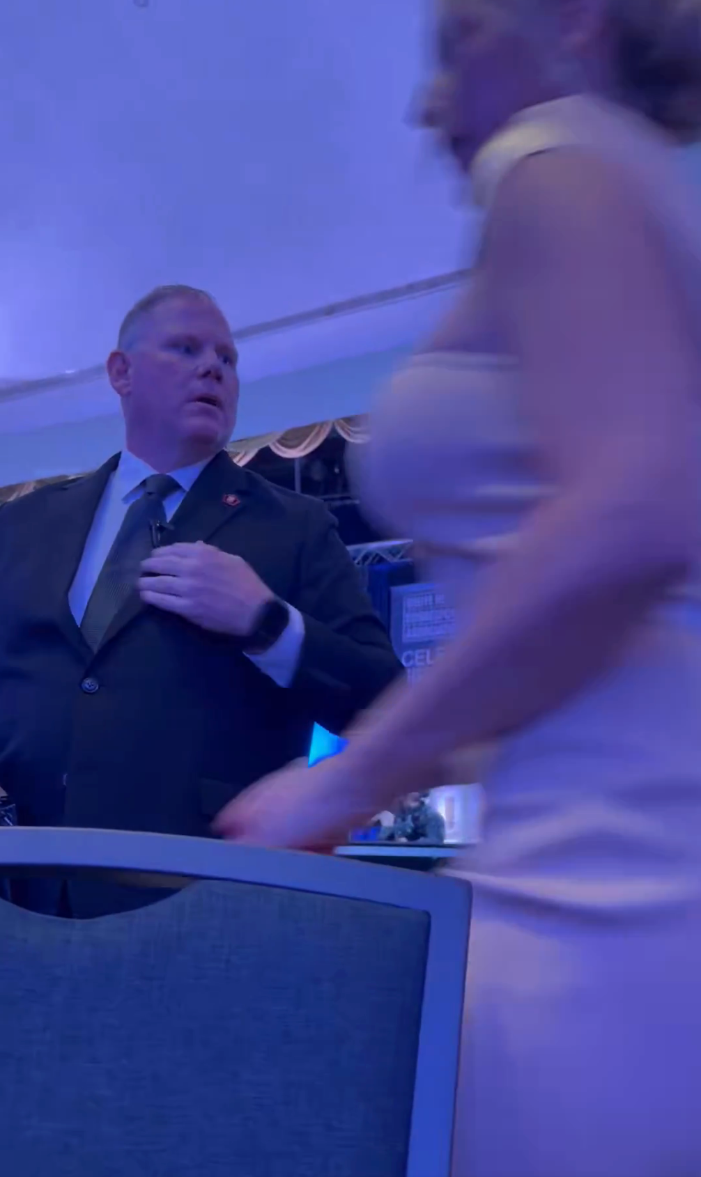 A idiosyncratic   successful  ceremonial  deterioration  stands successful  a dimly lit room, looking to the side, arsenic  different  idiosyncratic   walks by successful  a light-colored sleeveless dress