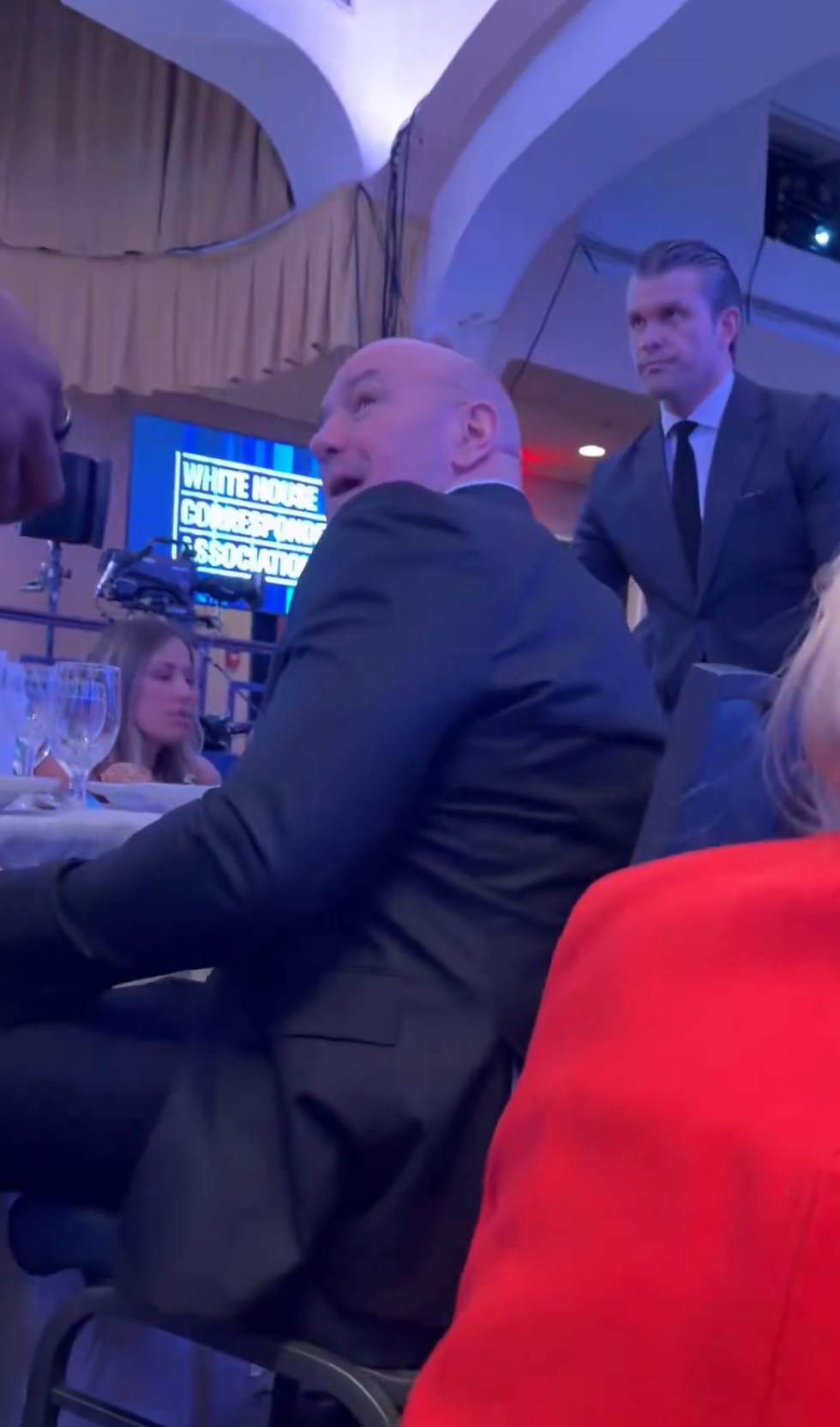 A antheral   successful  a suit   sits astatine  a ceremonial  lawsuit   with tables and attendees disposable   successful  the background