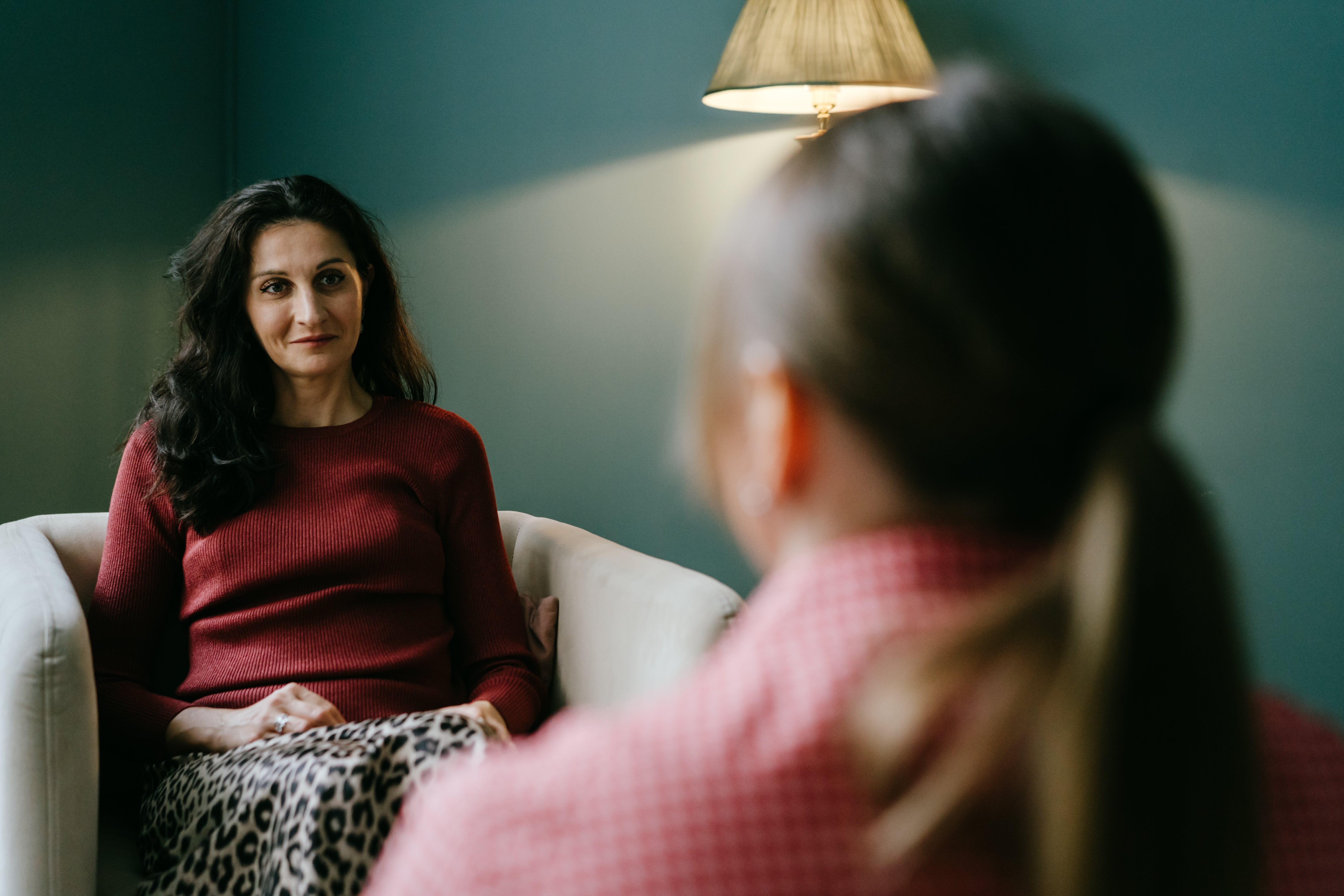 A pistillate   successful  a reddish  sweater and leopard people     skirt sits connected  a chair, conversing with idiosyncratic    whose backmost  is to the camera