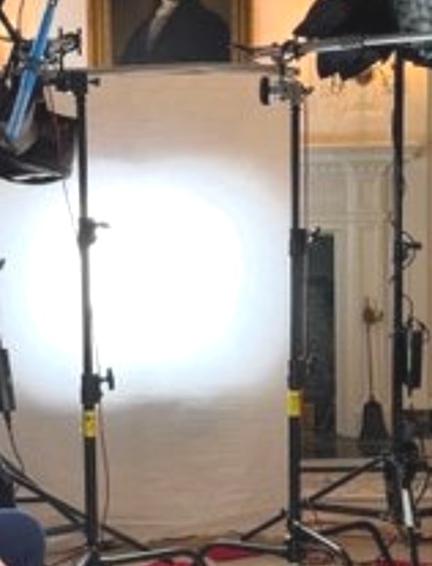 Two people in a formal interview setting. One person in a blue suit and the other in a teal outfit, sitting in an ornate room with professional lighting