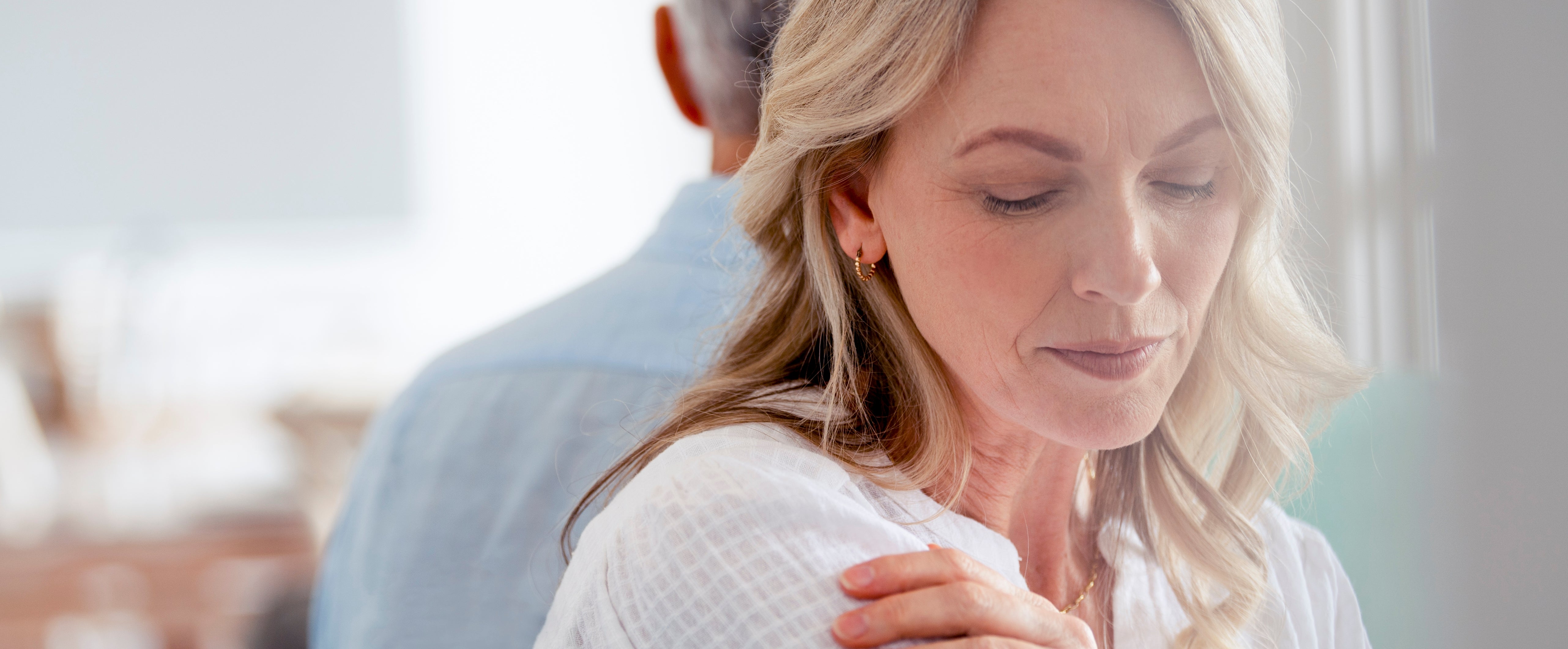 A pistillate   with closed eyes and a thoughtful look  sits adjacent   a window, mildly  touching her shoulder, with different  idiosyncratic   seated down  her