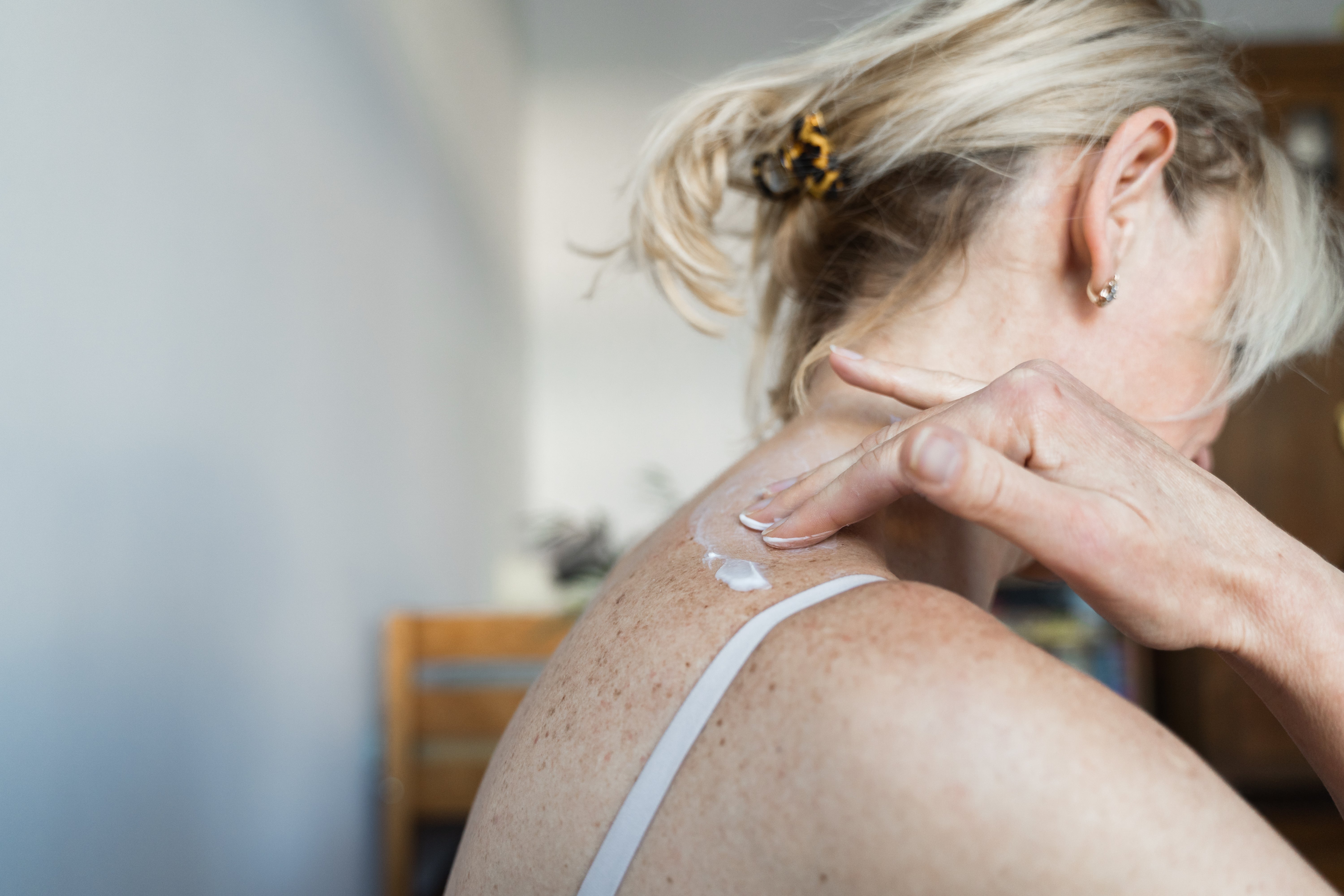 Person applying lotion to their shoulder, wearing a vessel  top. Hair is up   with a hairsbreadth  clip