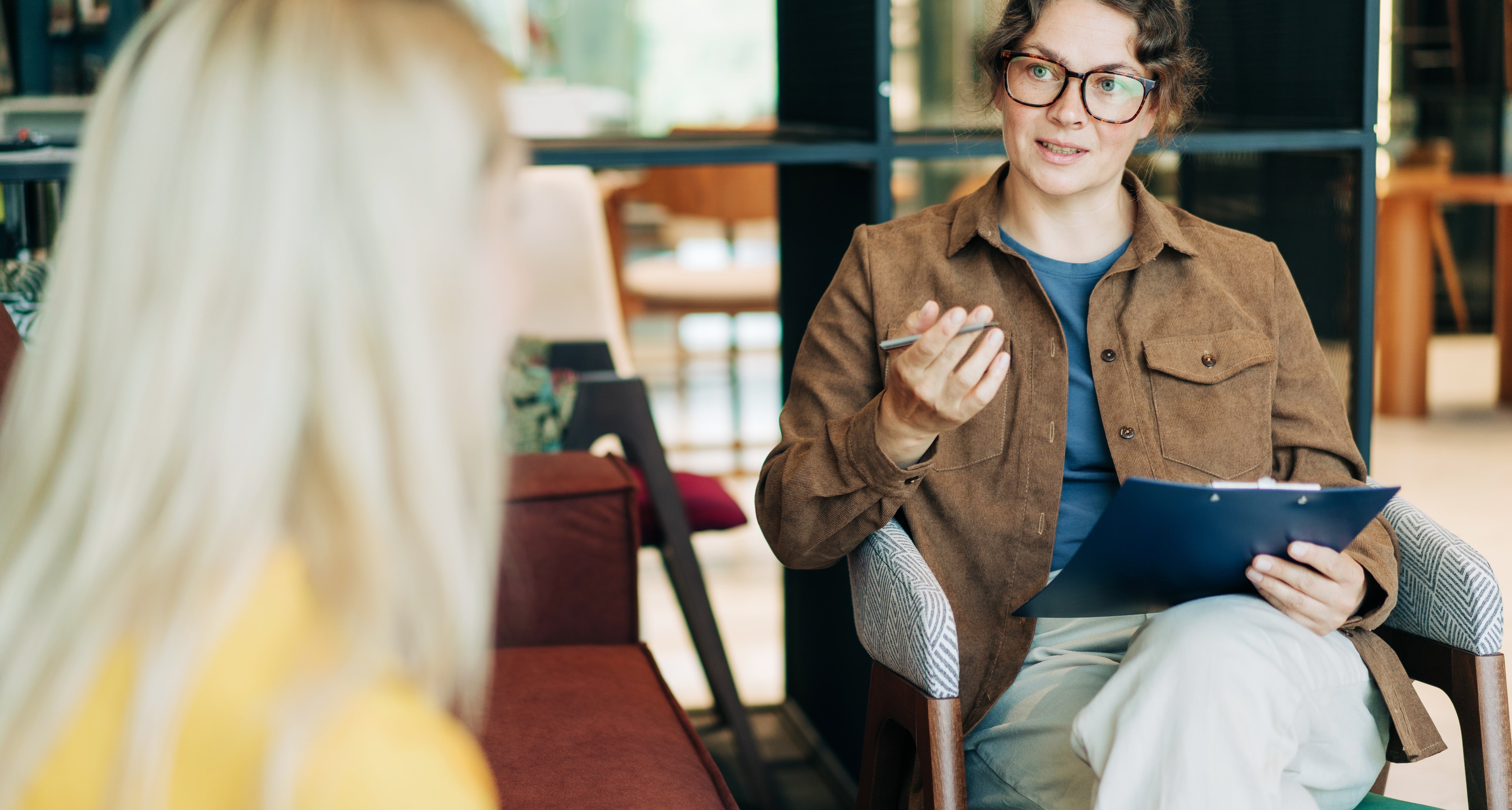 Person successful  glasses and casual attire sitting with clipboard, listening attentively to different  idiosyncratic   successful  a casual setting