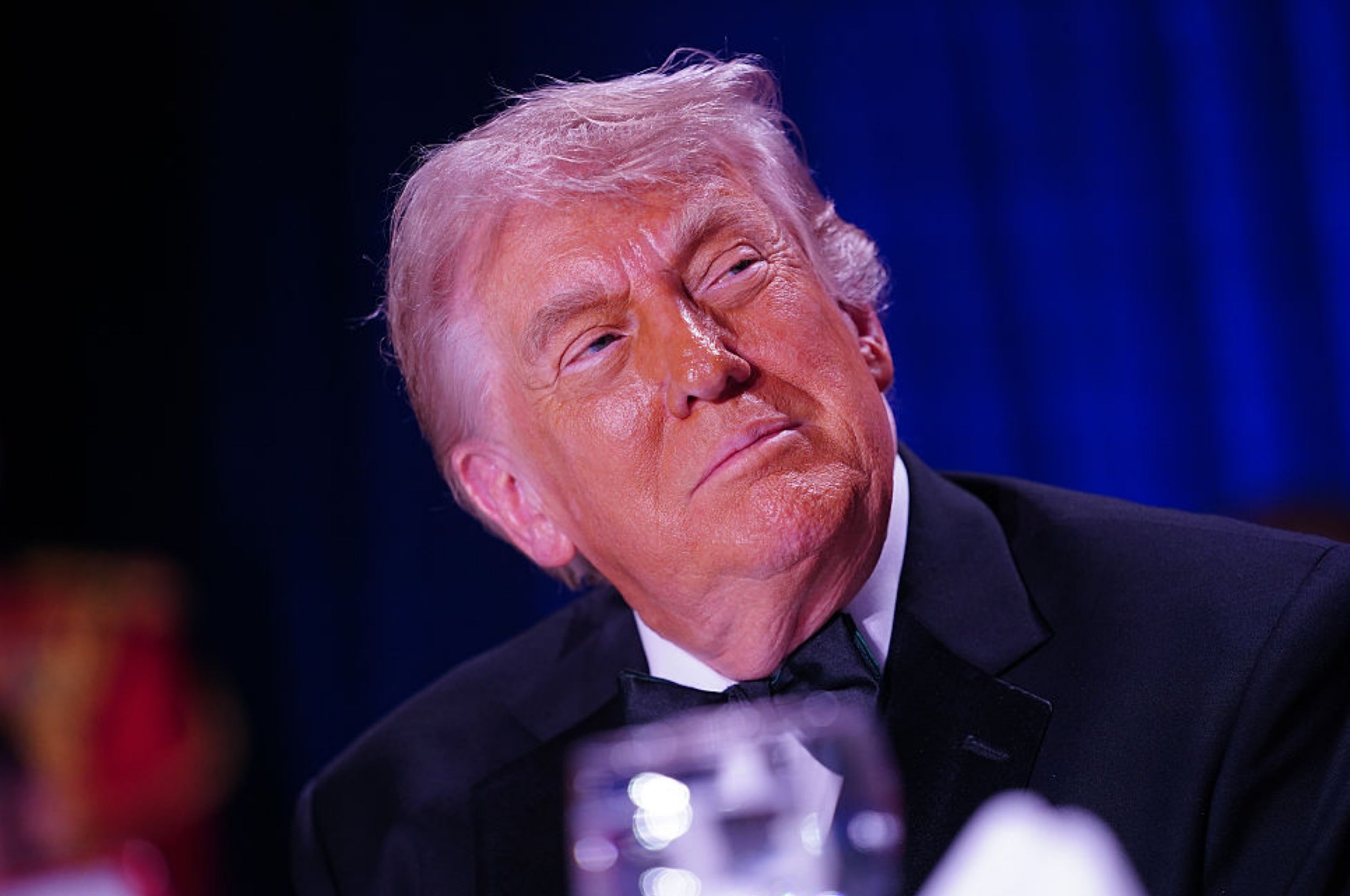trump in formal attire, sitting at an event, looking thoughtfully towards the side