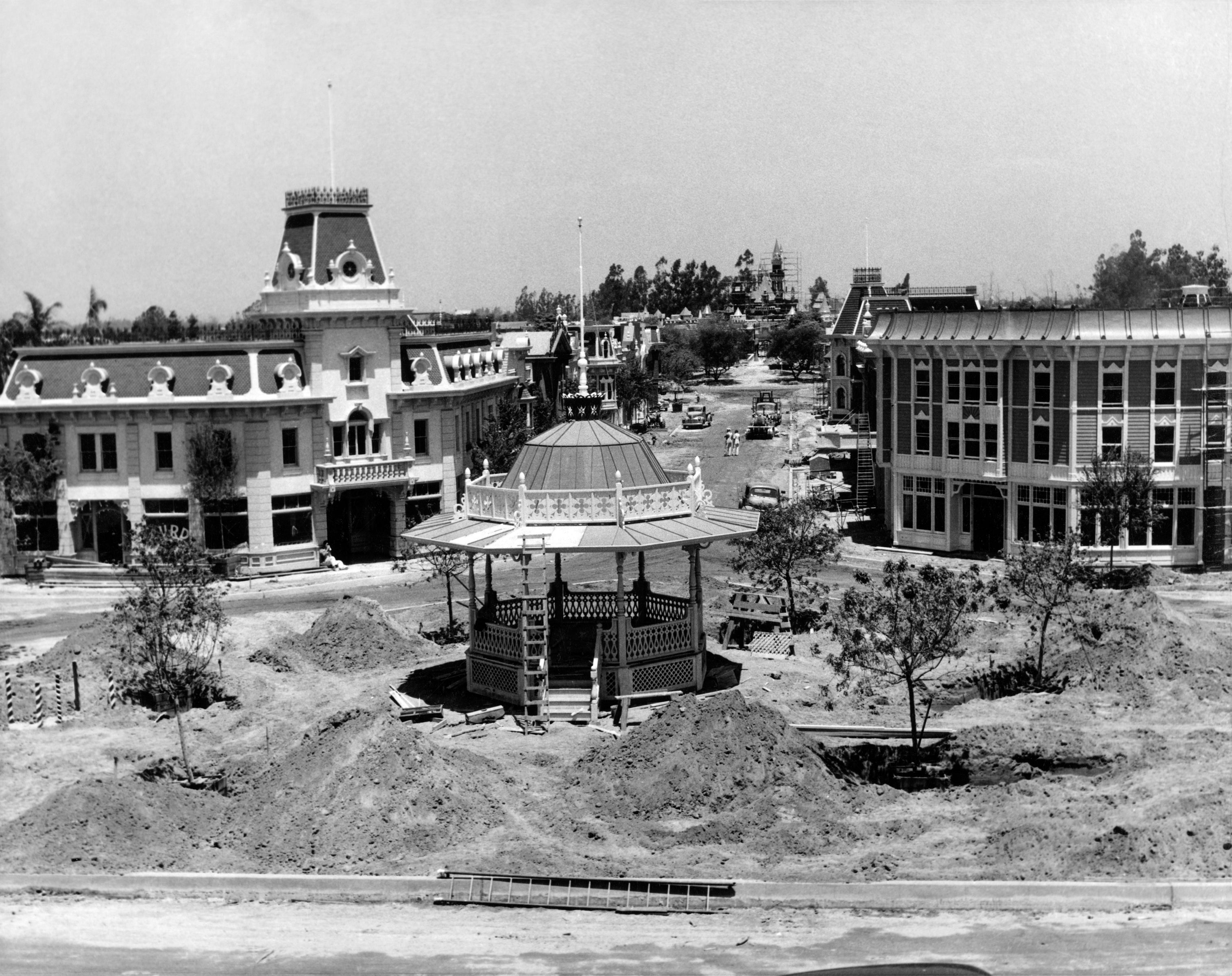 Historical photograph  of Disneyland nether  construction, featuring Main Street U.S.A. with unfinished structures and a cardinal  gazebo surrounded by dirt