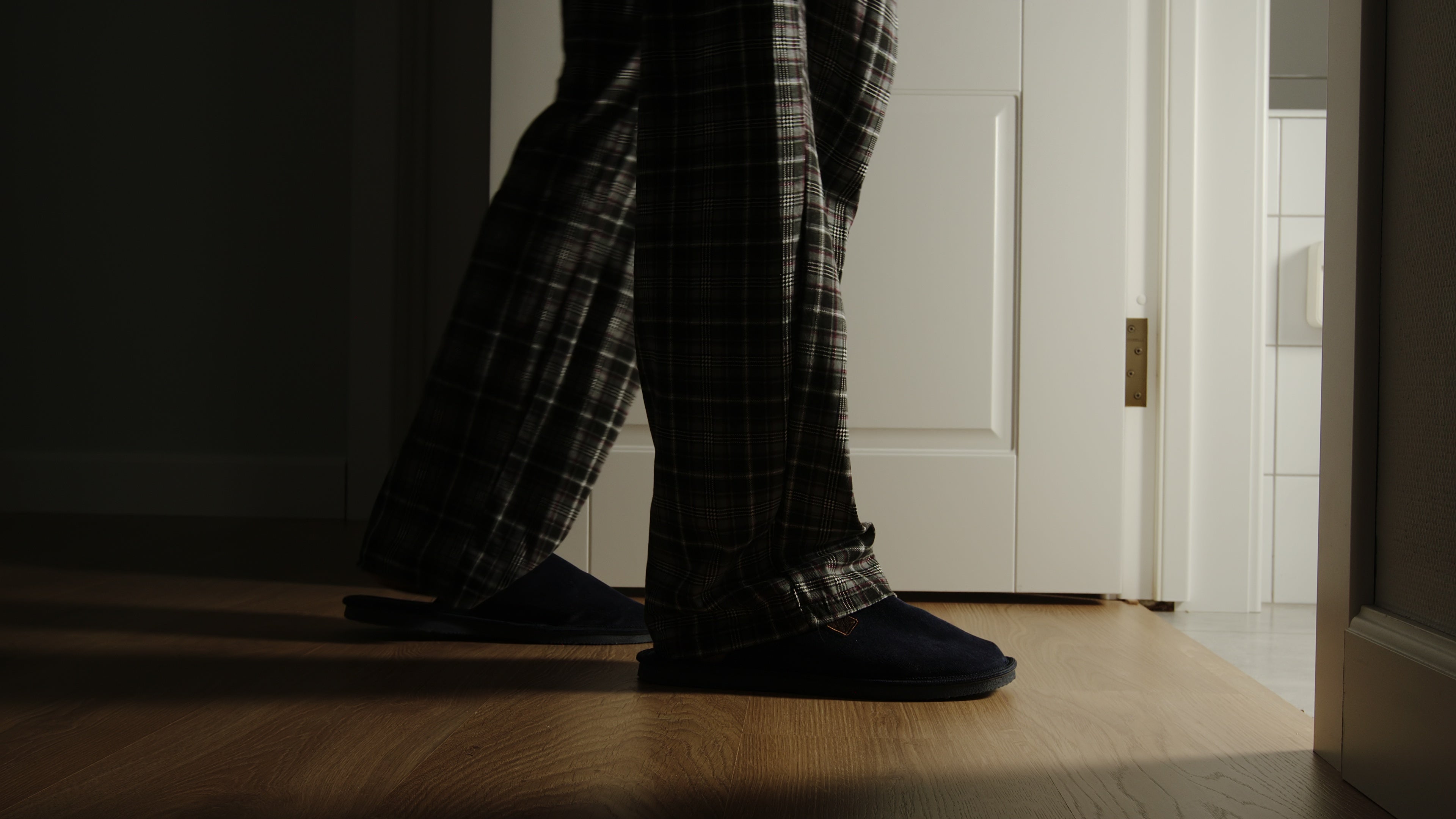 A idiosyncratic   wearing plaid pajama pants and slippers walks towards an unfastened  door, with airy  coming from wrong  the room