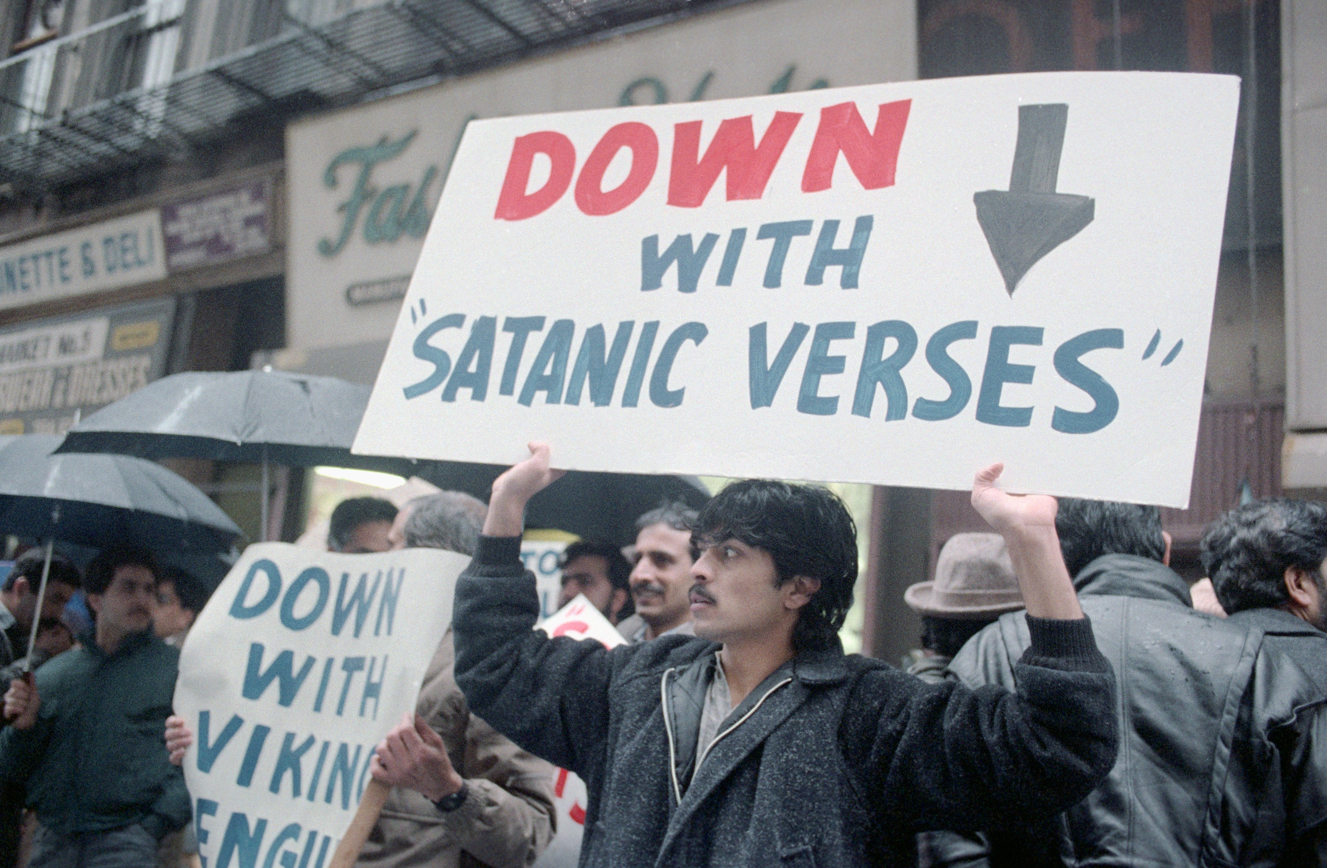 Protesters clasp  signs against the publication  "Satanic Verses," with 1  prominently speechmaking  "Down with 'Satanic Verses'," during a thoroughfare  demonstration